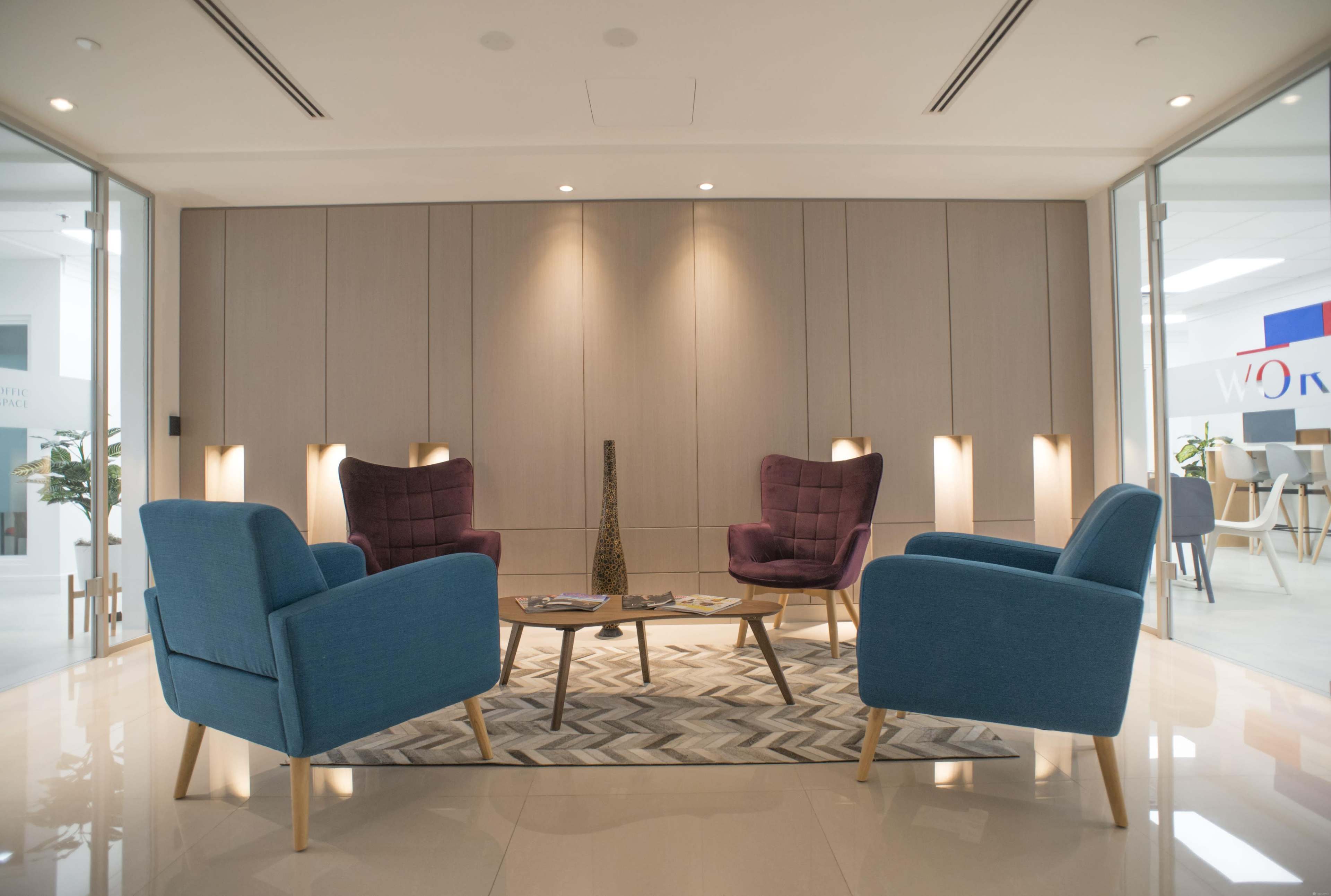 A modern lounge area with four armchairs arranged around a central table on a patterned rug, against a backdrop of wooden paneling and ambient lighting.
