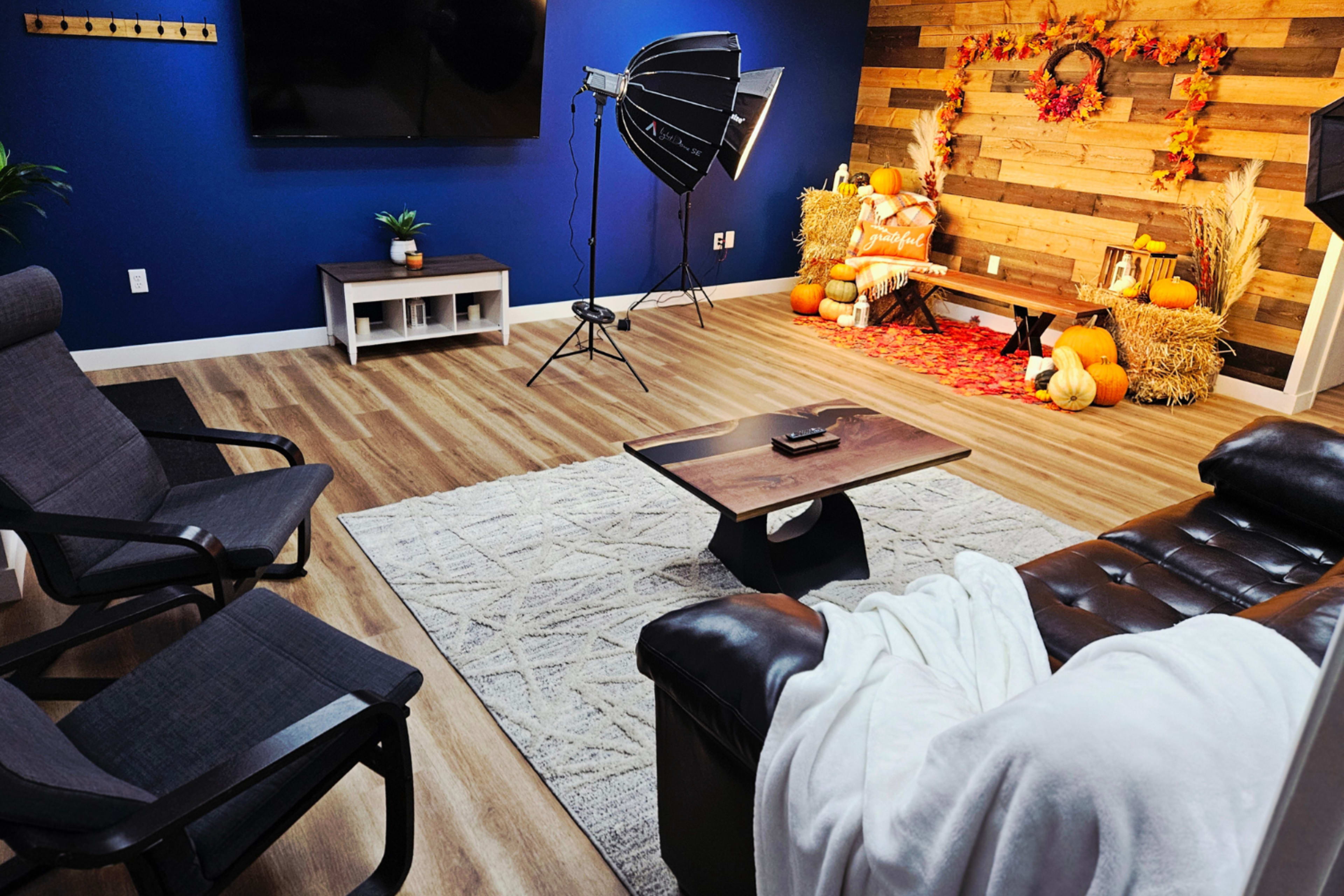 The room features a cozy seating area with dark chairs and a leather couch, surrounded by a backdrop decorated with pumpkins and autumn-themed decor.
