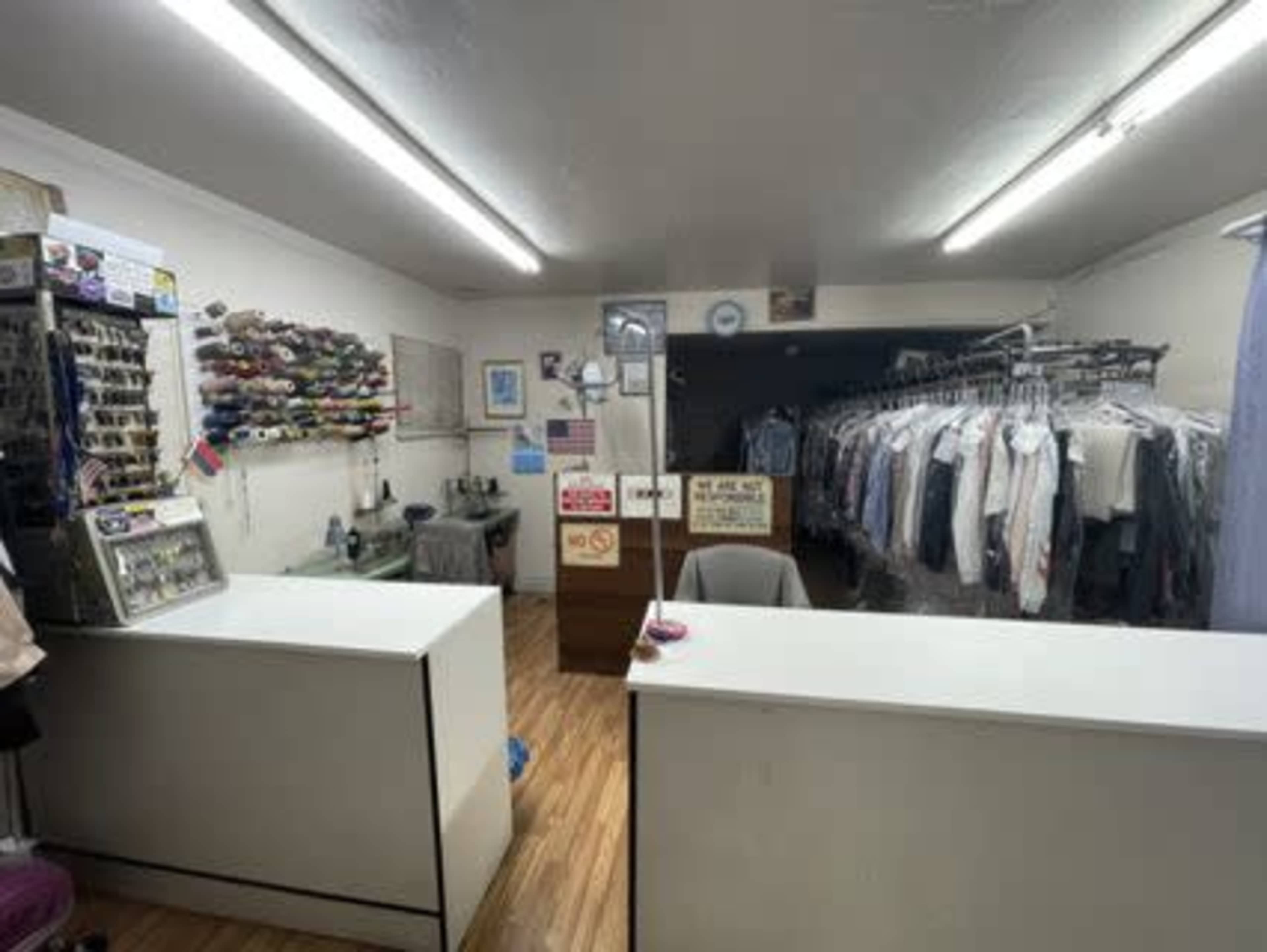 The image shows the interior of a clothing alteration shop with garment racks displaying various garments and a front counter.