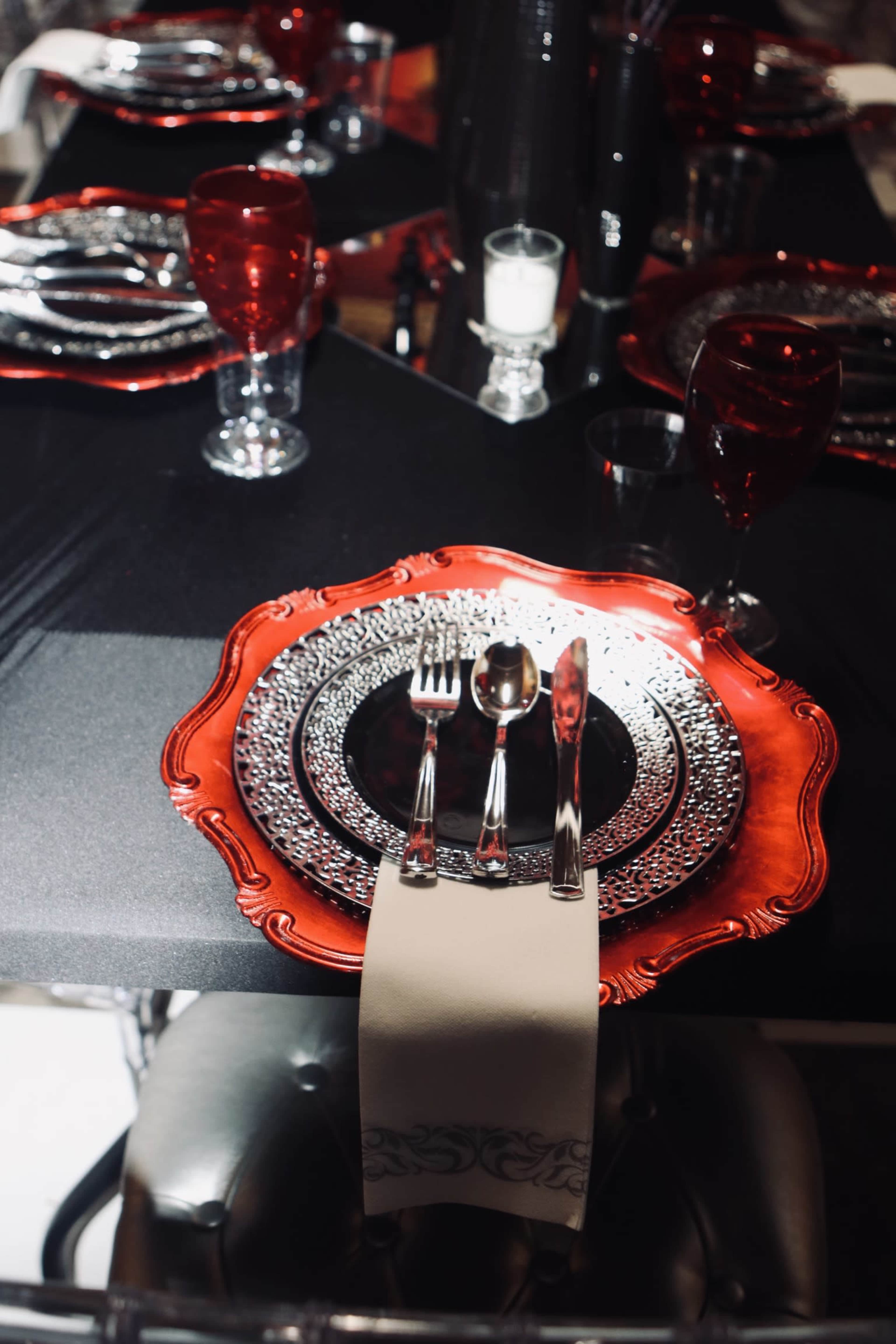 A beautifully arranged dining table set with red and silver plates, sparkling glassware, and neatly placed cutlery on a black tablecloth.