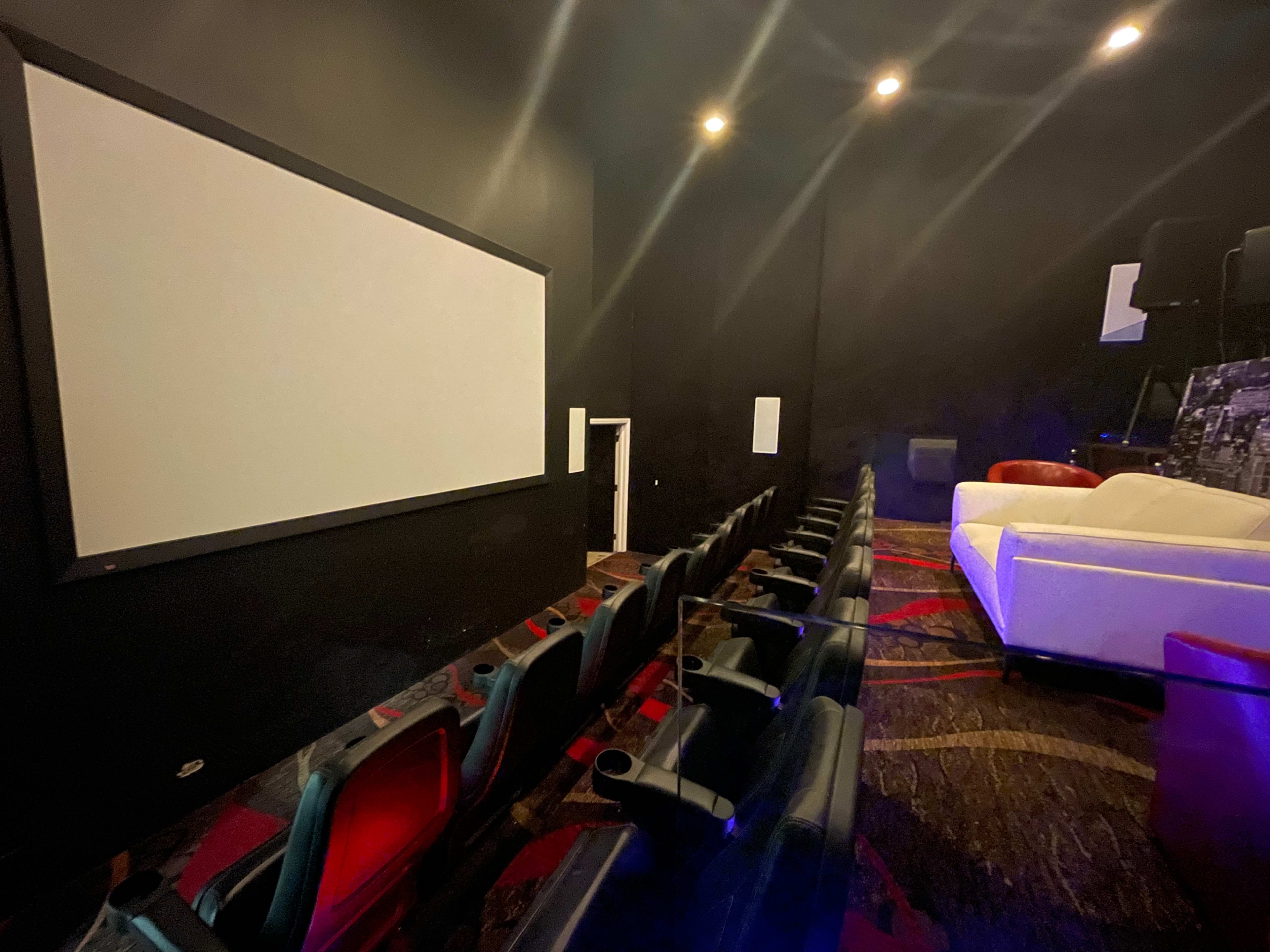 A small home theater features a blank screen, rows of black seats, and a white couch along the back wall.