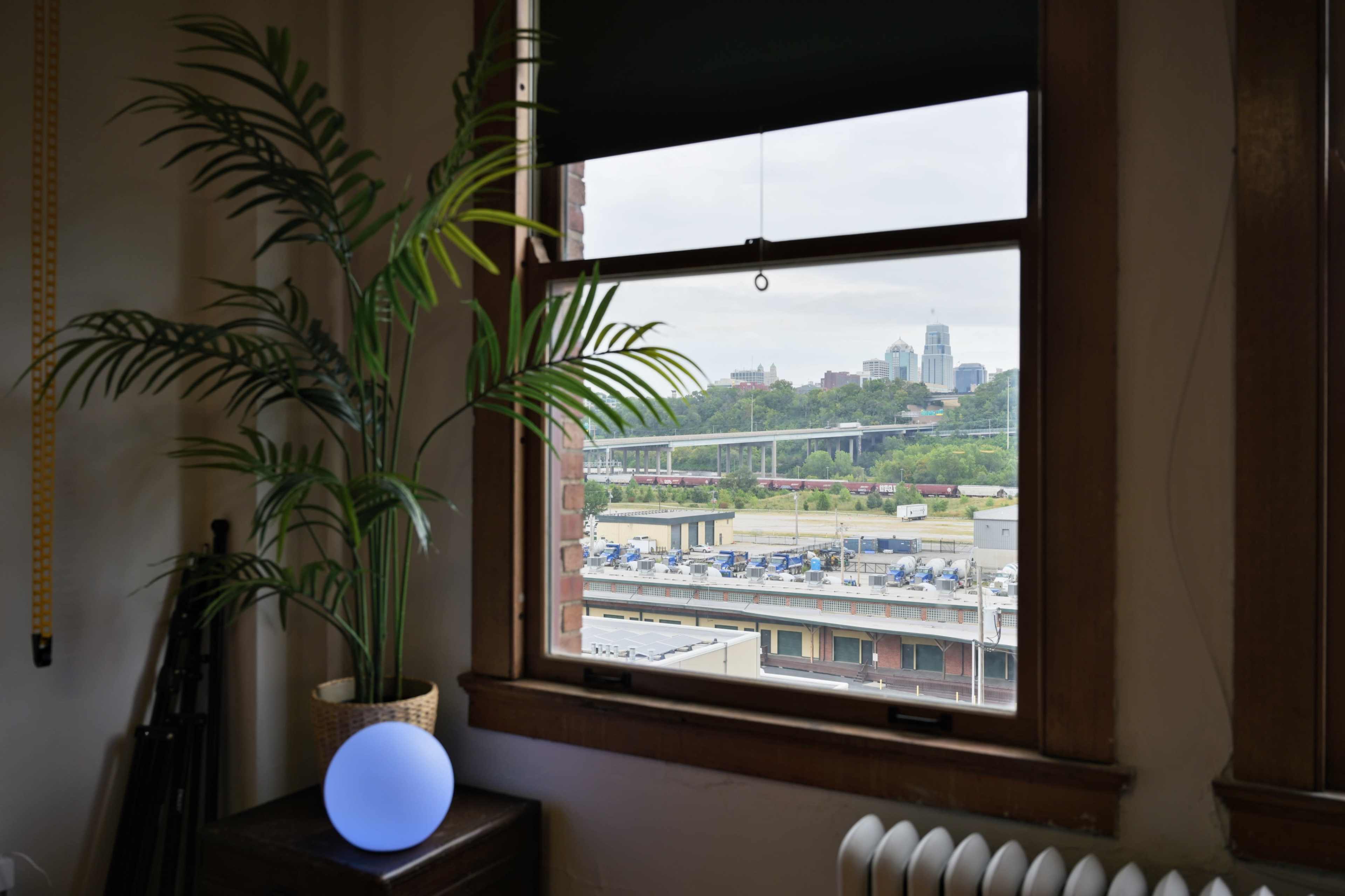The image shows a view from a window with a potted plant, a glowing blue sphere, and a city skyline in the background.