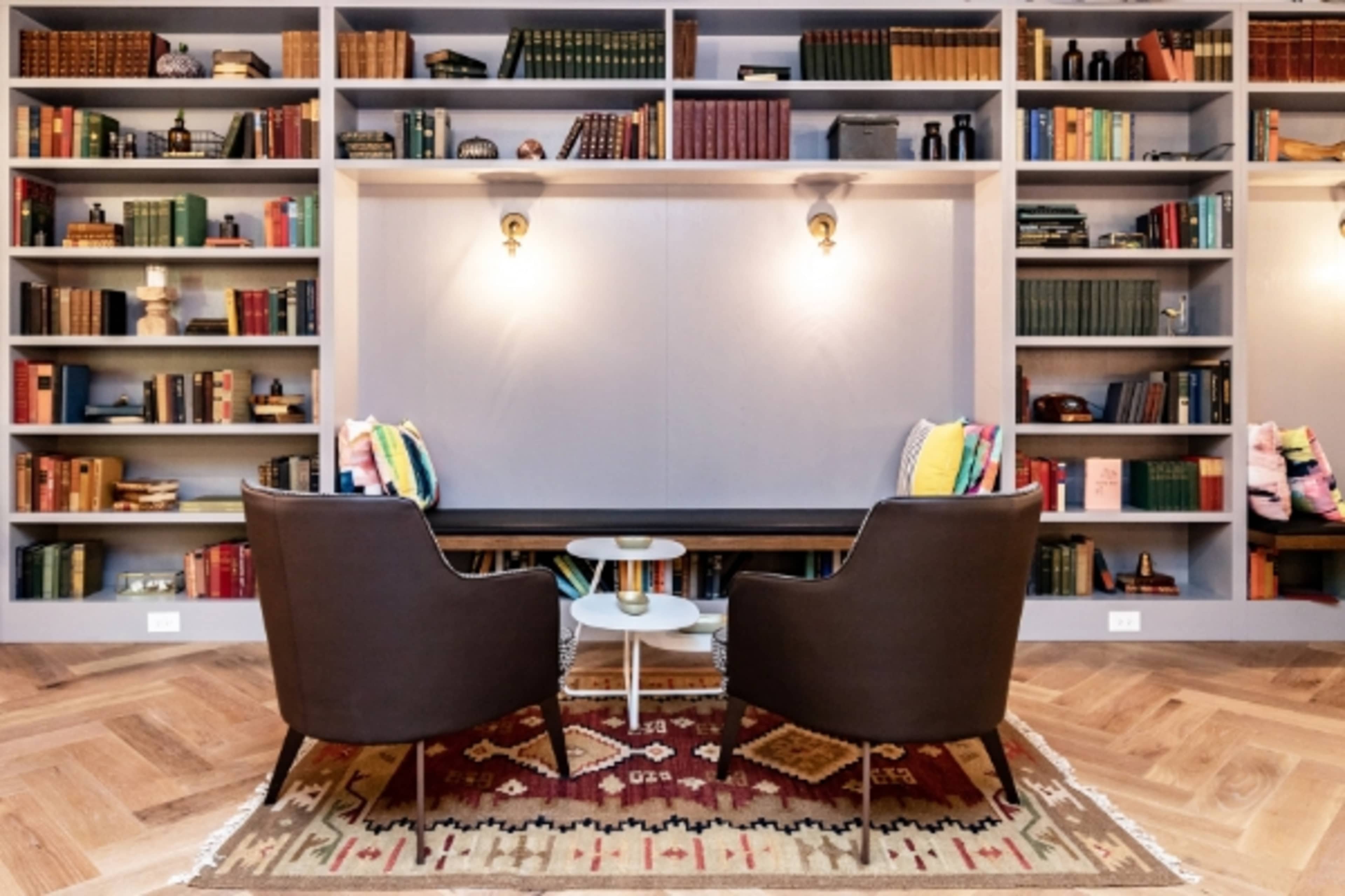 A cozy reading nook with two chairs flanking a small table in front of a large bookshelf filled with books.