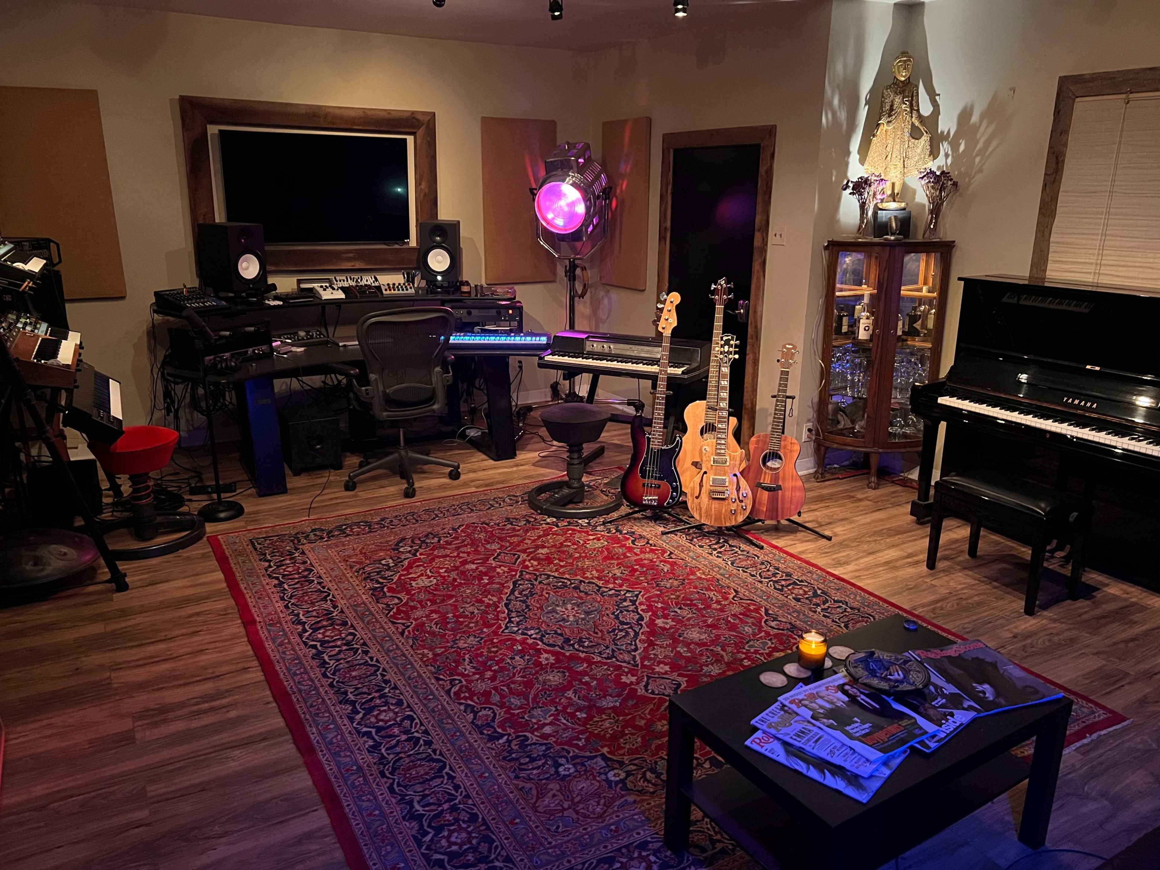 A home music studio featuring various instruments, including guitars and a piano, surrounded by a decorative rug and a section with studio equipment.