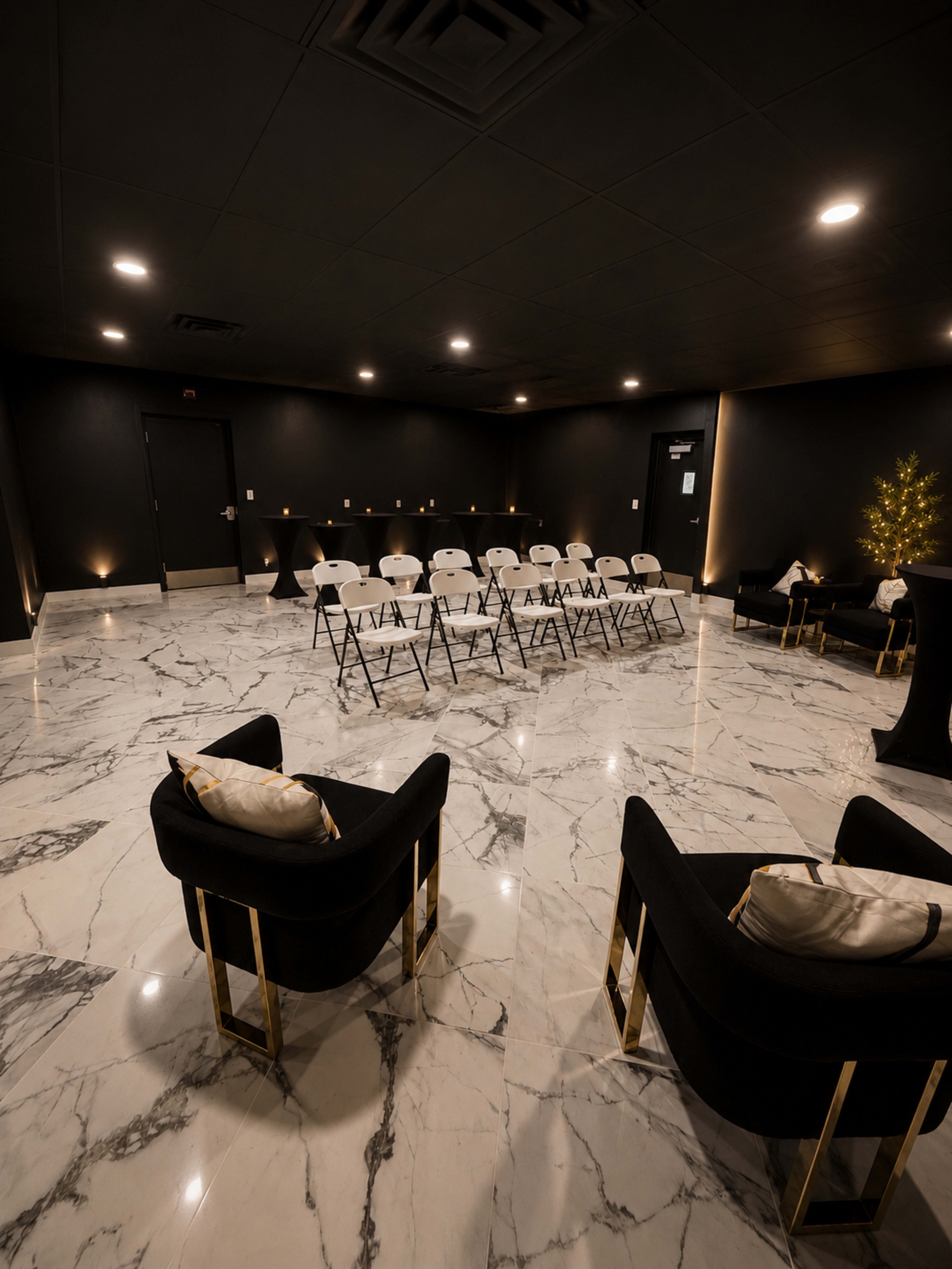 The image shows a modern meeting room with black chairs arranged in rows on a marble floor, accented by elegant lighting.