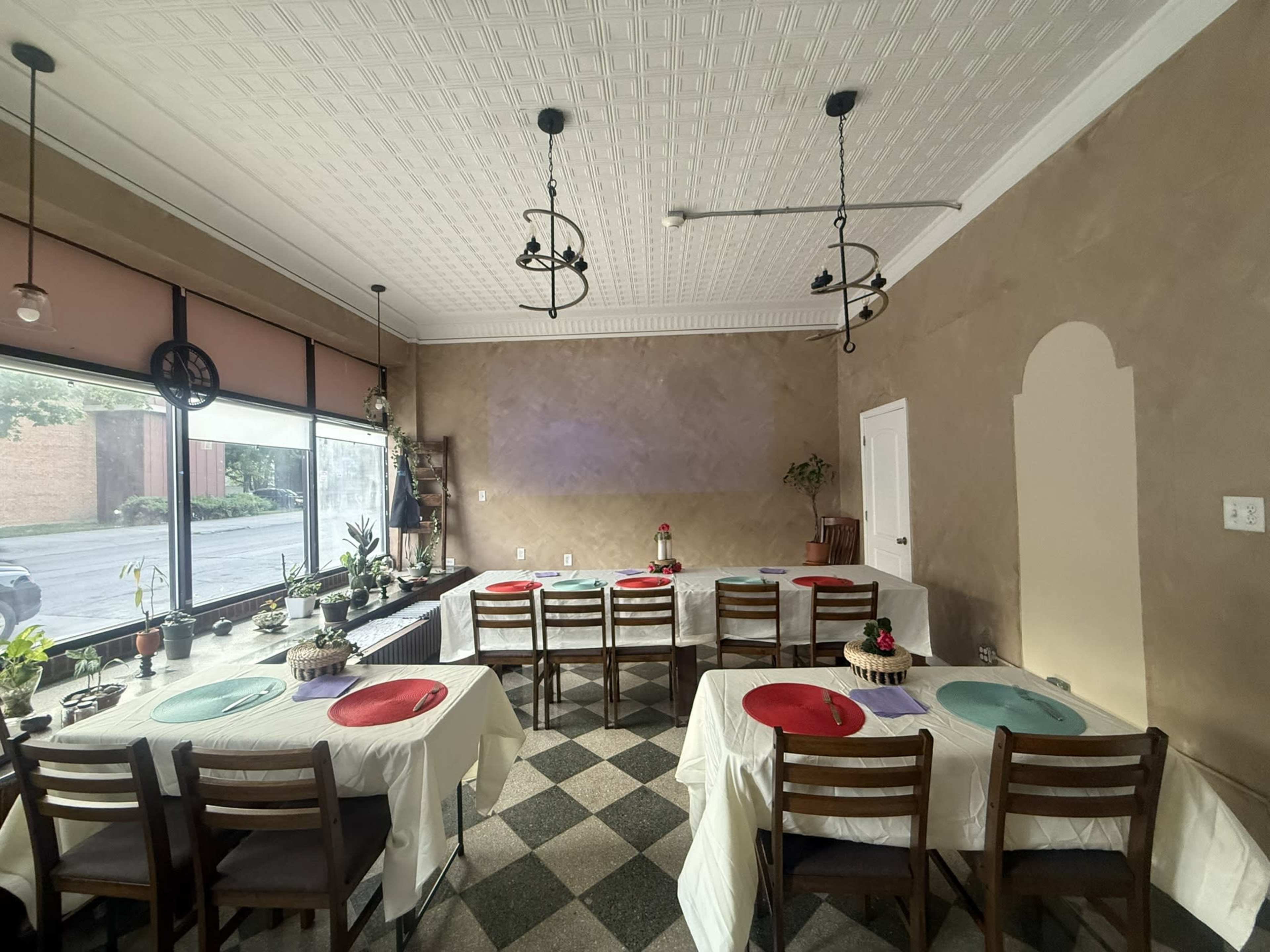 The image shows a dining area with several tables set with colorful tablecloths and a large window providing natural light.