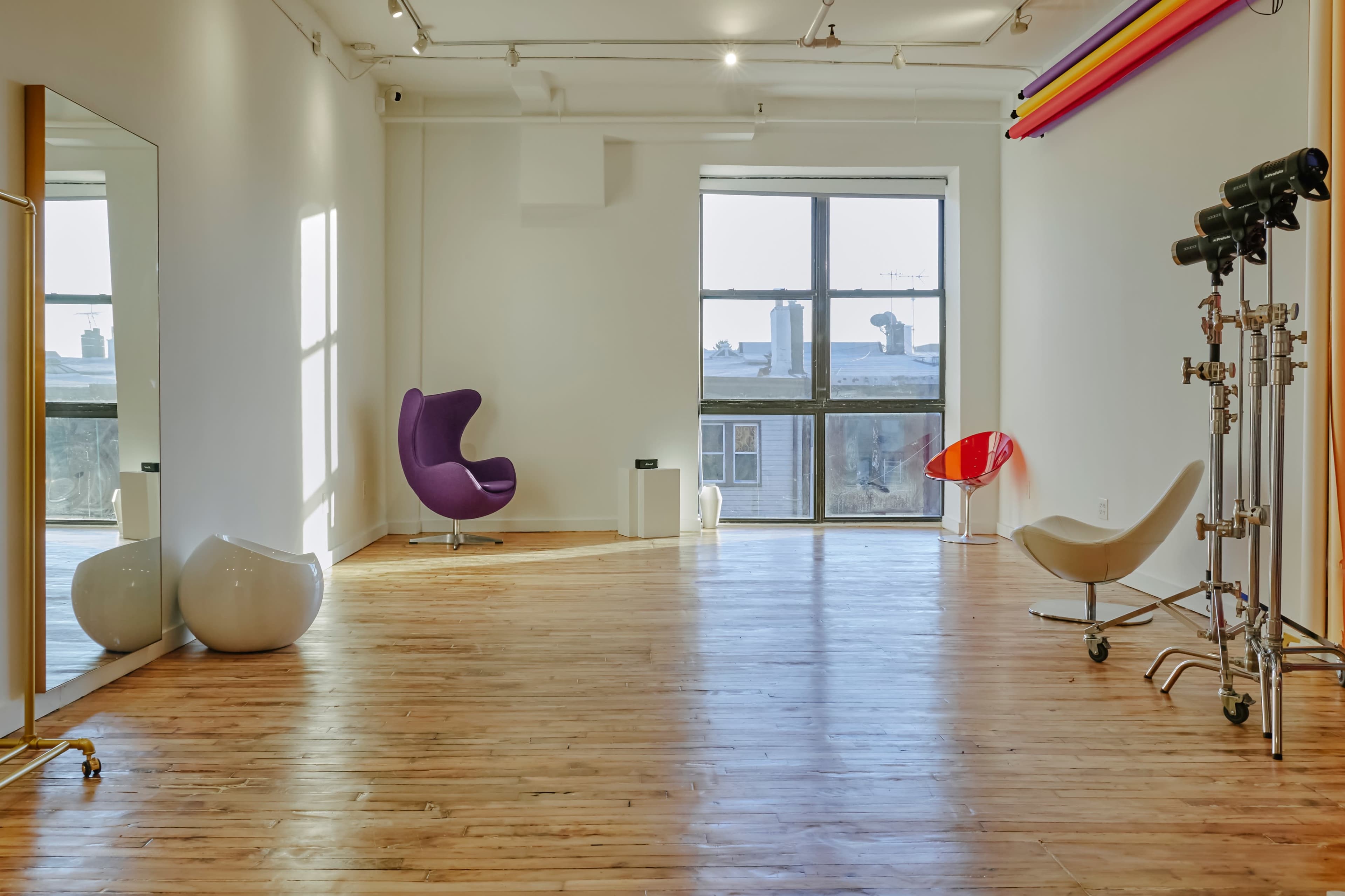 A spacious, well-lit room with wooden floors, featuring a large window and modern furniture, including a purple chair and an oval-shaped white object.