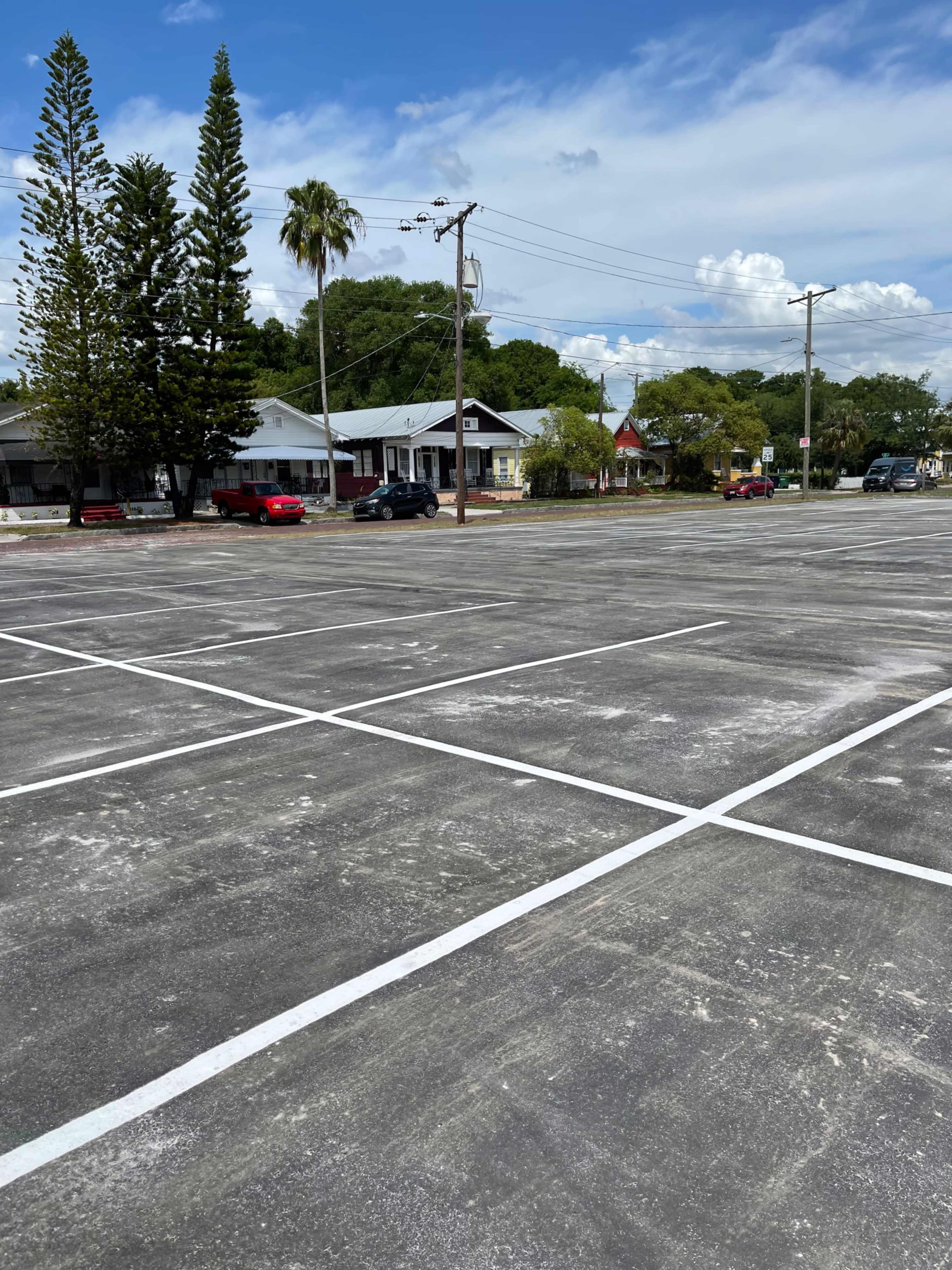 An empty parking lot with freshly marked lines, surrounded by a few houses and trees.