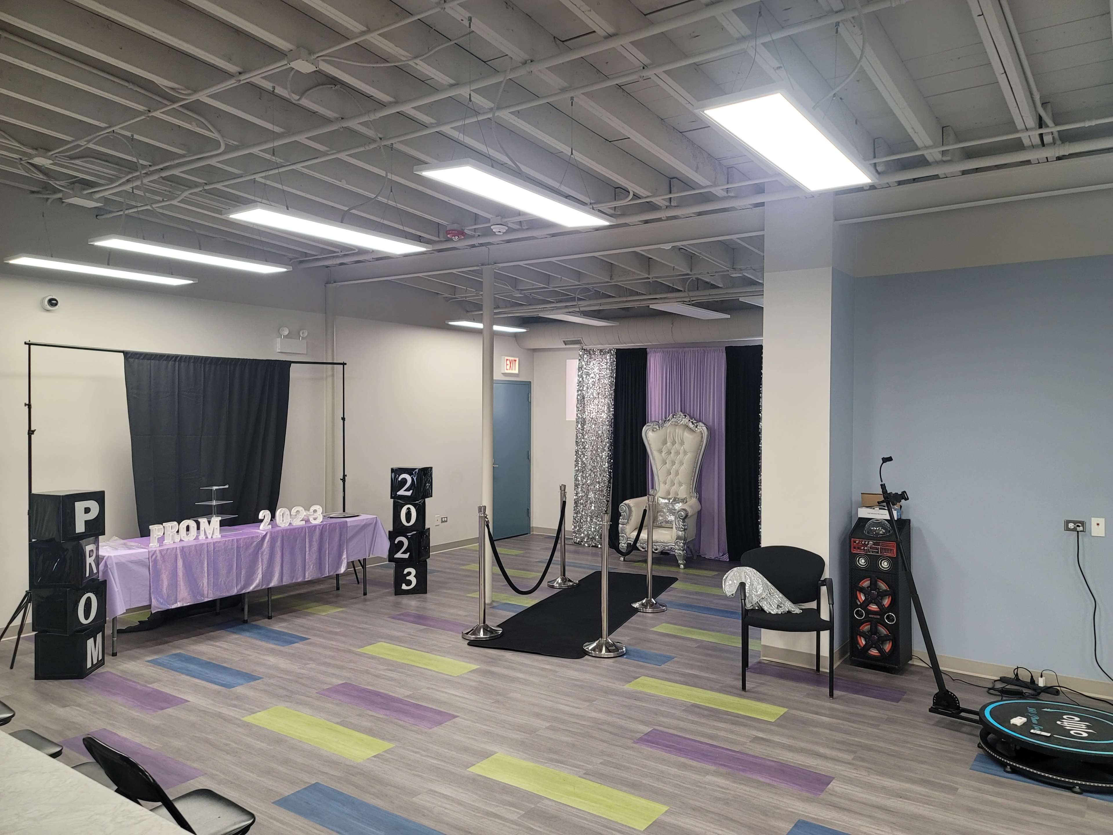 The room is set up for a prom event, featuring a decorated table with "PROM 2023" signage, a throne-like chair, and a red carpet with velvet ropes.