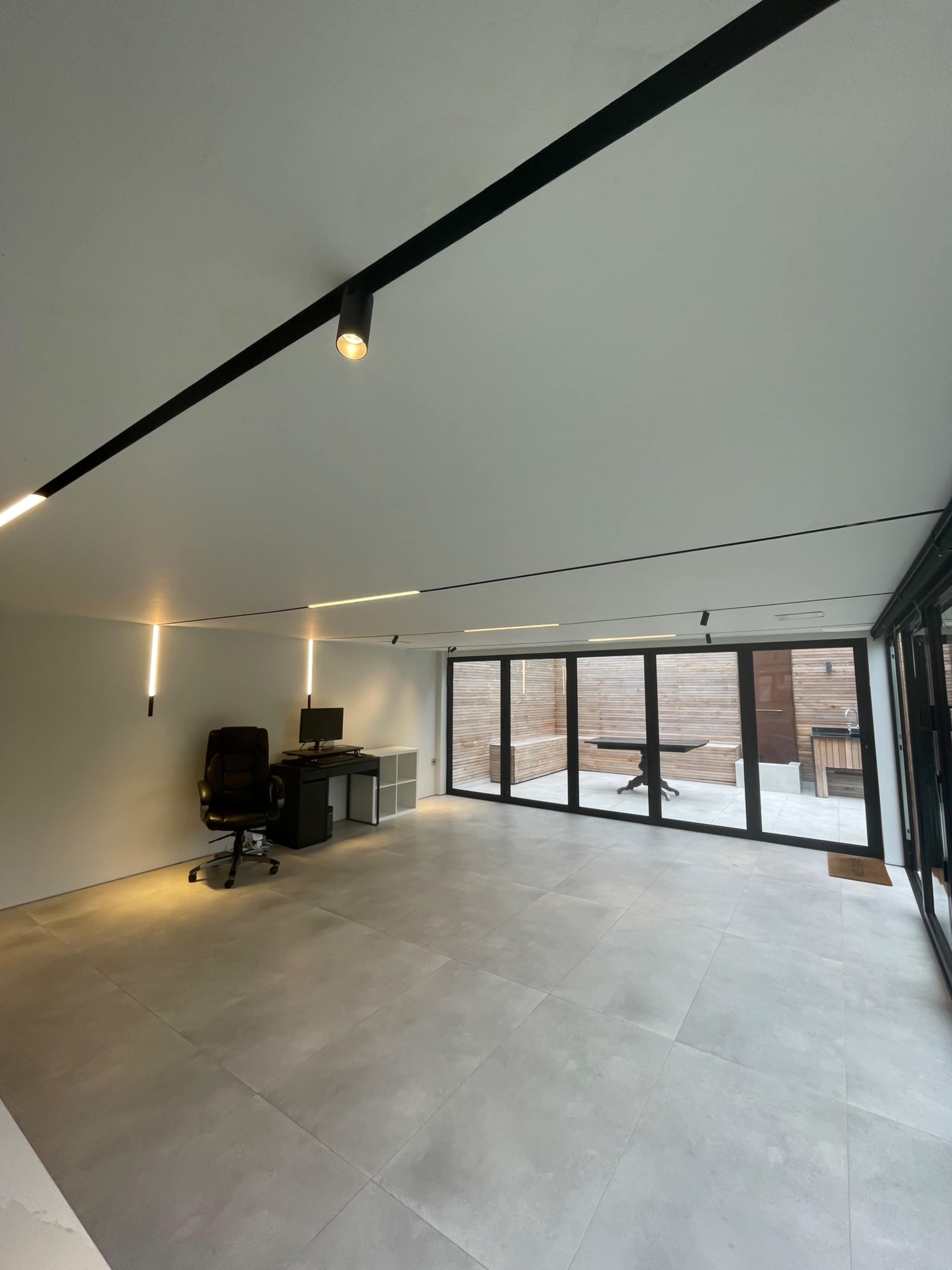 A spacious, modern office with a large window wall, minimalist furniture, and polished concrete flooring.
