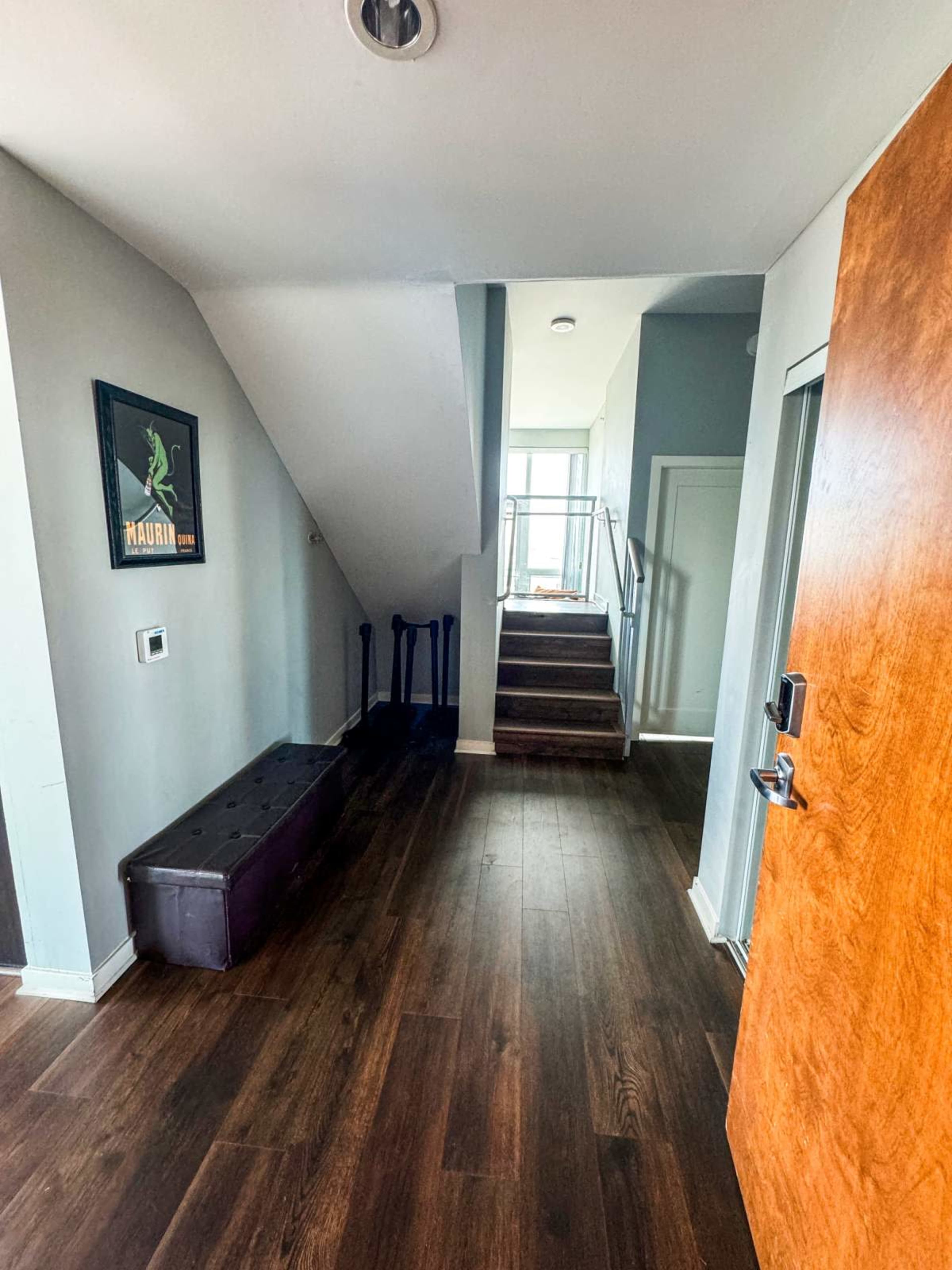 A hallway with a wooden floor, a staircase leading up, and a bench against the wall near the entrance.