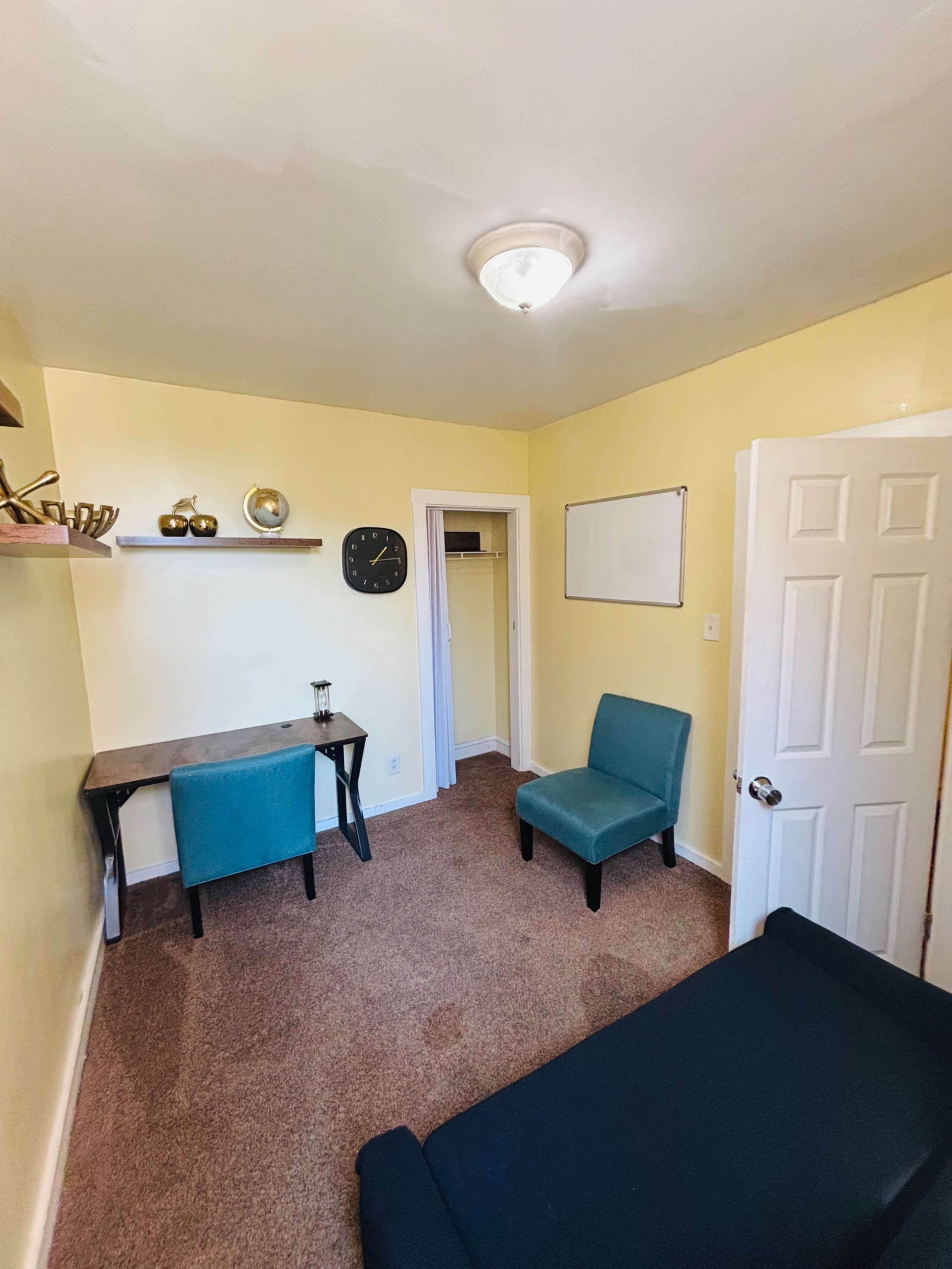 The image shows a small room with yellow walls, a desk and chair, a clock on the wall, and a nearby closet.