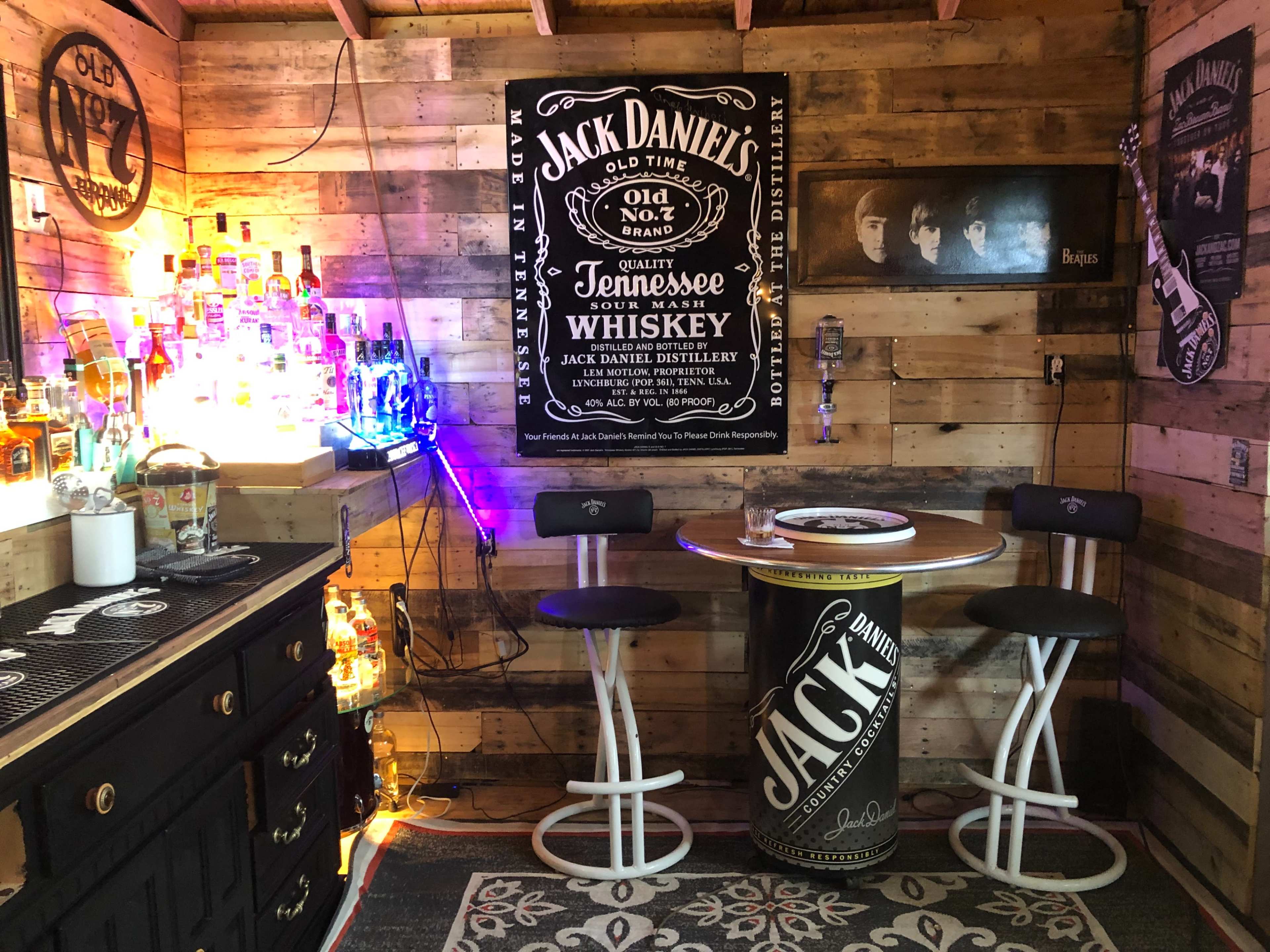 A rustic home bar featuring a wooden interior, a round bar table with stools, and various bottles of liquor displayed on shelves.