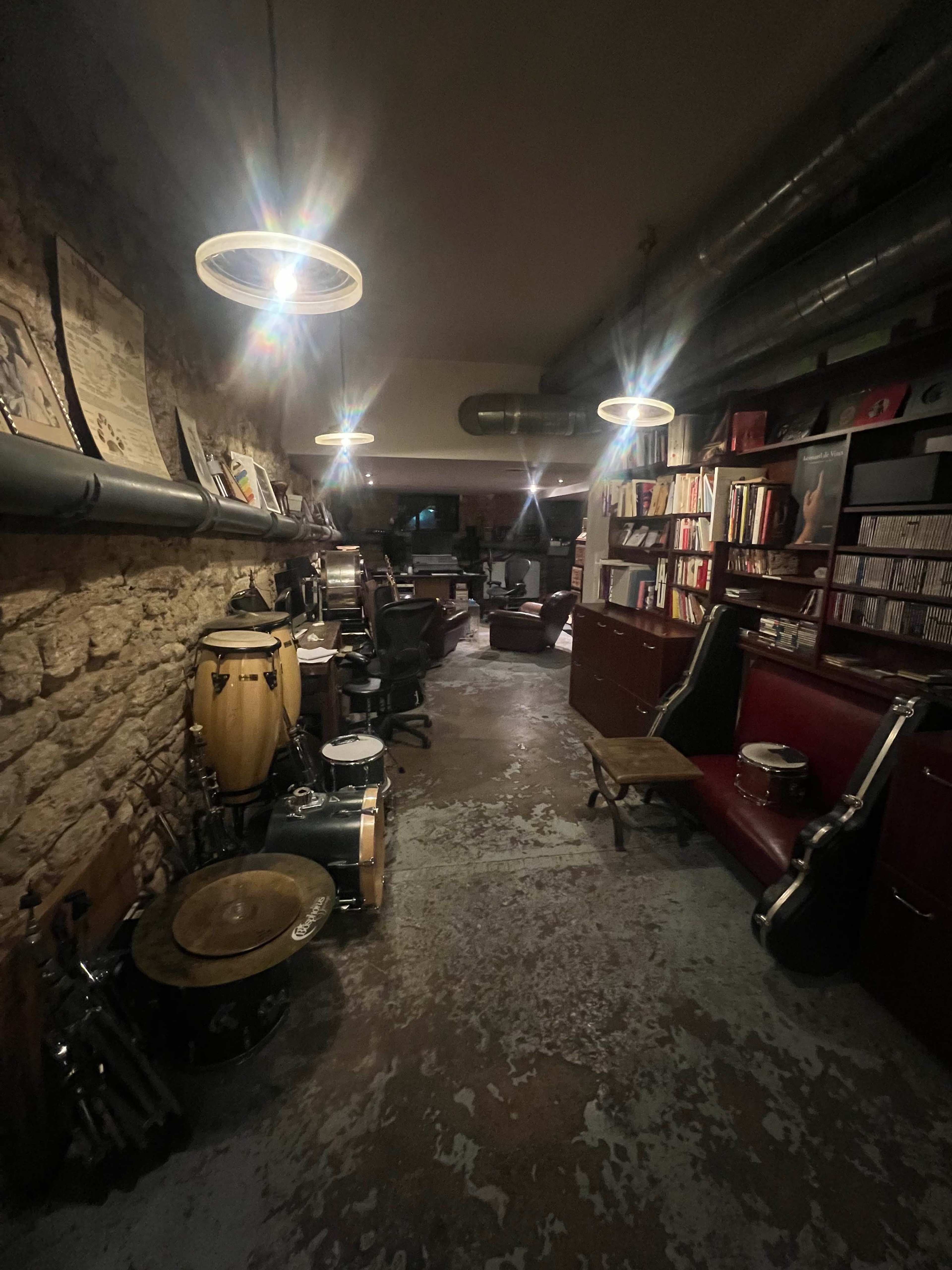 A dimly lit music studio with stone walls, various musical instruments, and shelves filled with records and books.