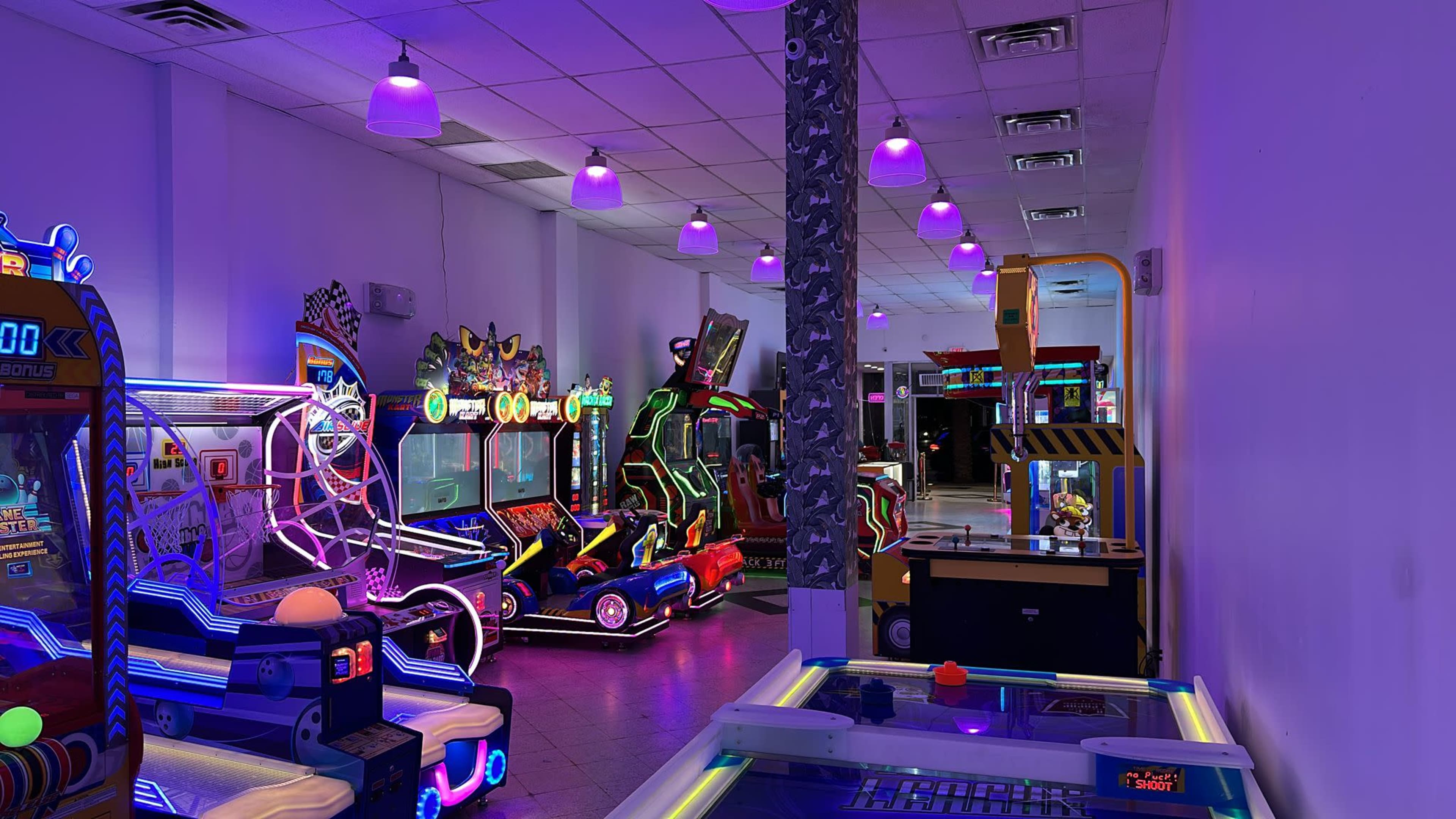 The image shows an arcade filled with various gaming machines illuminated by colorful neon lights.