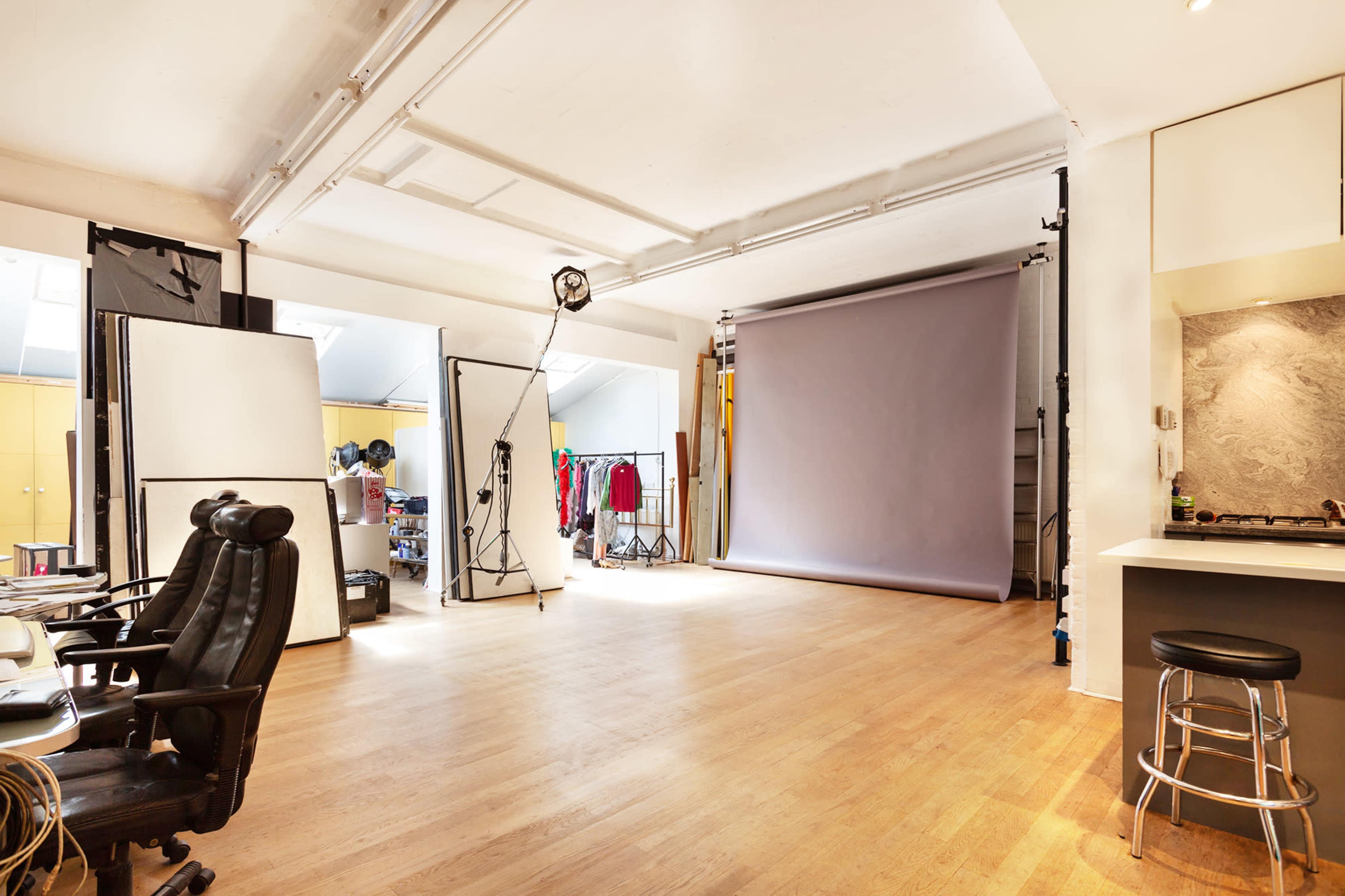 A spacious photography studio with a gray backdrop, lighting equipment, and various props and clothing racks in a well-organized setting.