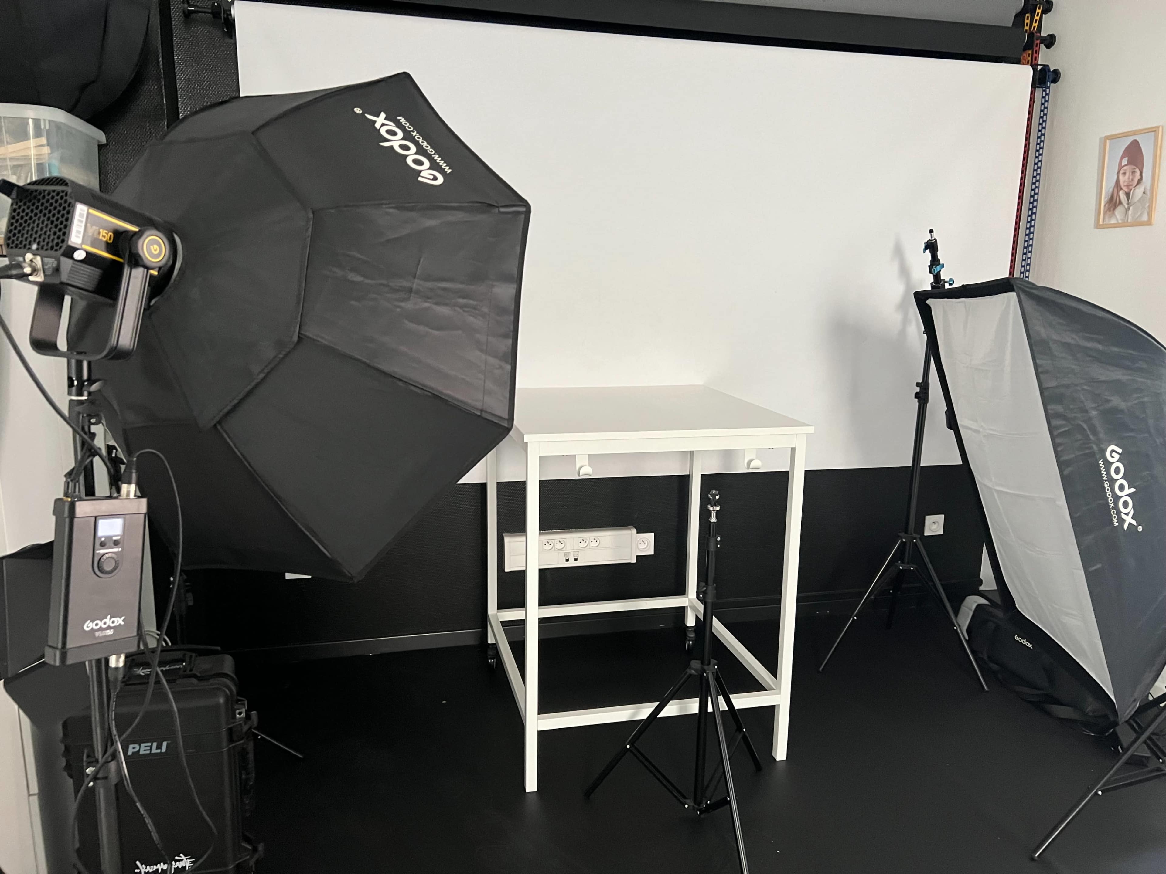 A photography studio setup with two softbox lights, a white backdrop, and a table positioned in the center.