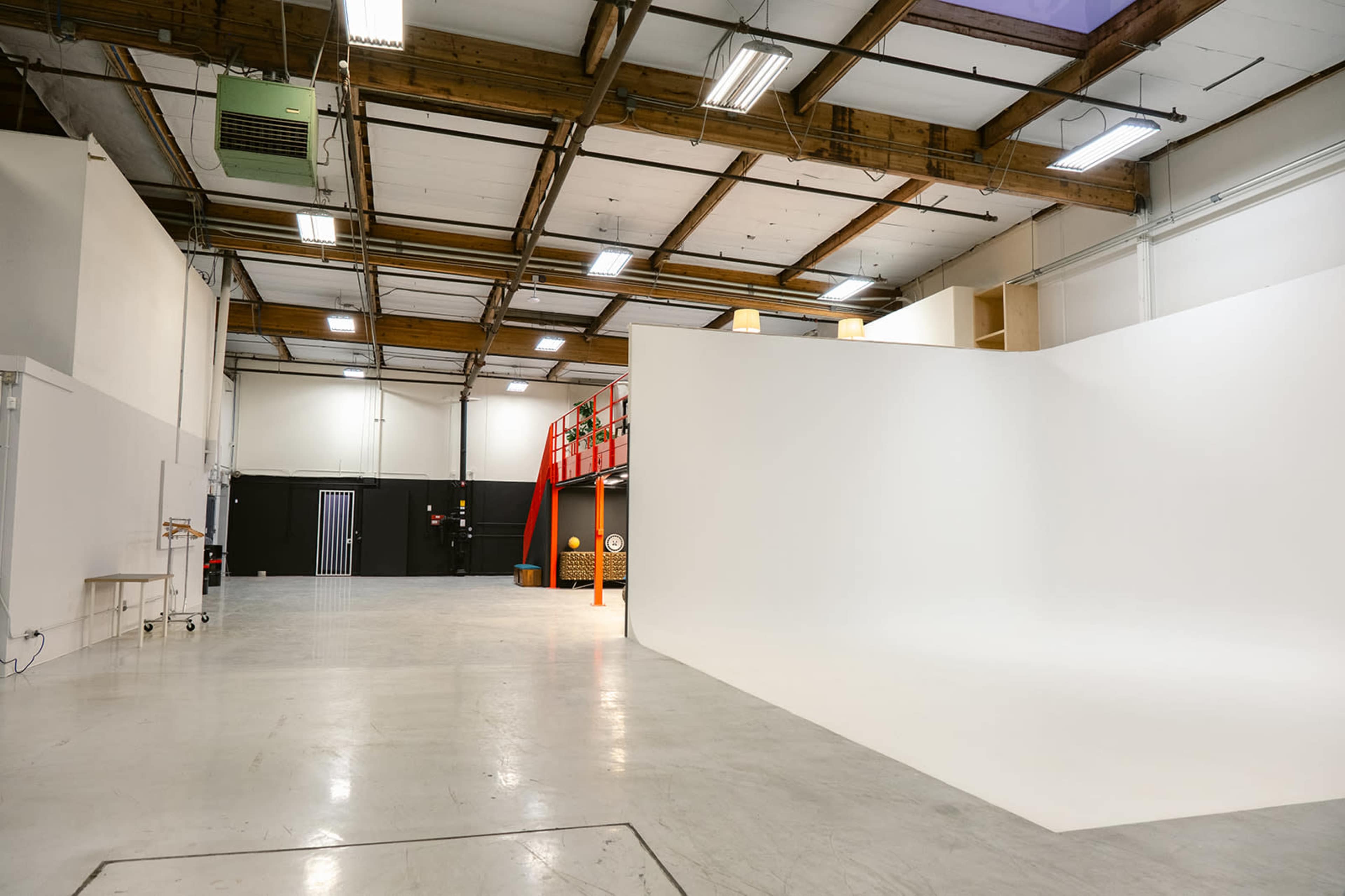 The image shows a vast, empty studio space with white walls and a smooth floor, illuminated by overhead lights.