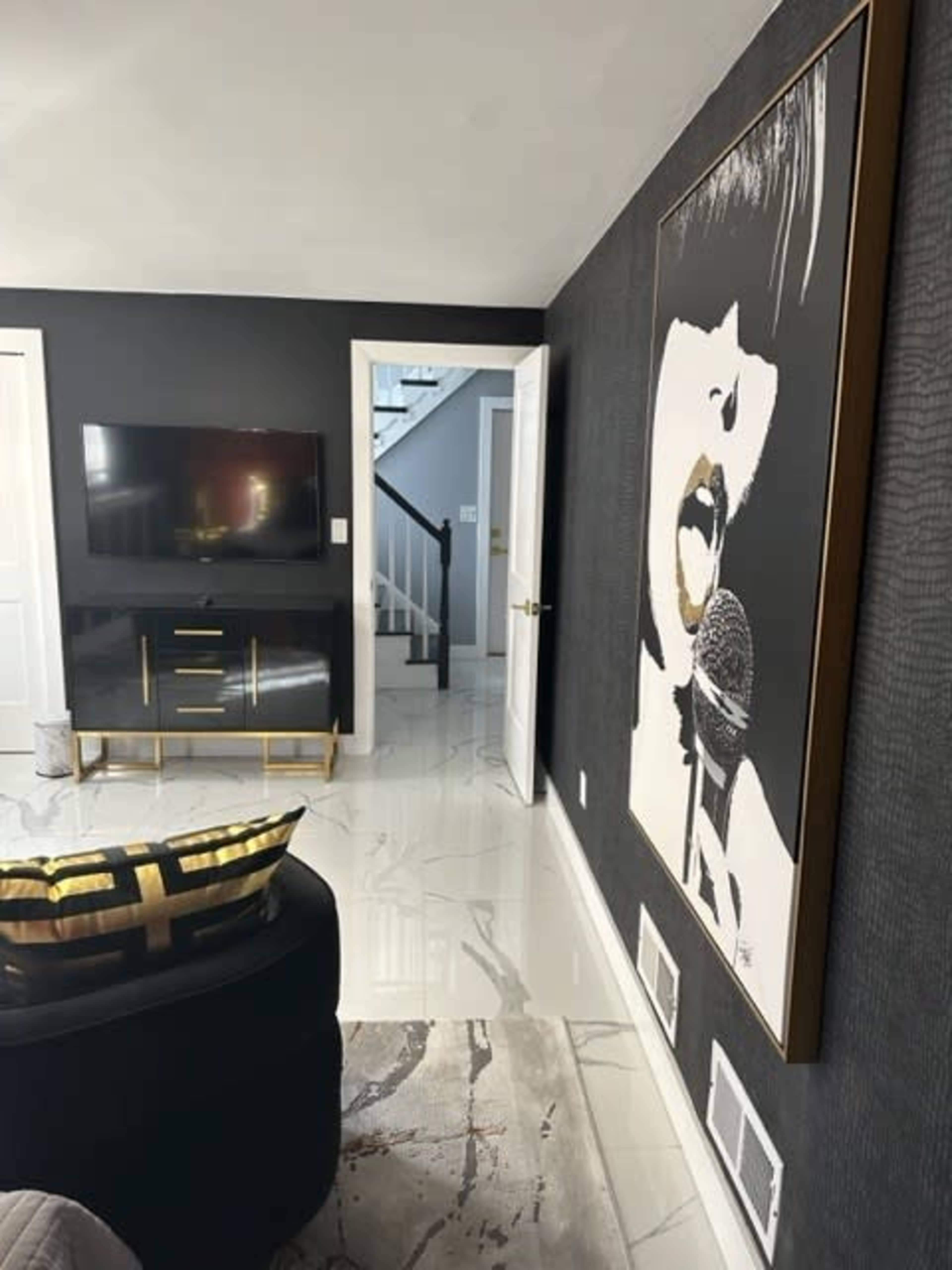A modern living space with a black and white artwork of a singer on the wall, a television on a console, and a staircase in the background.
