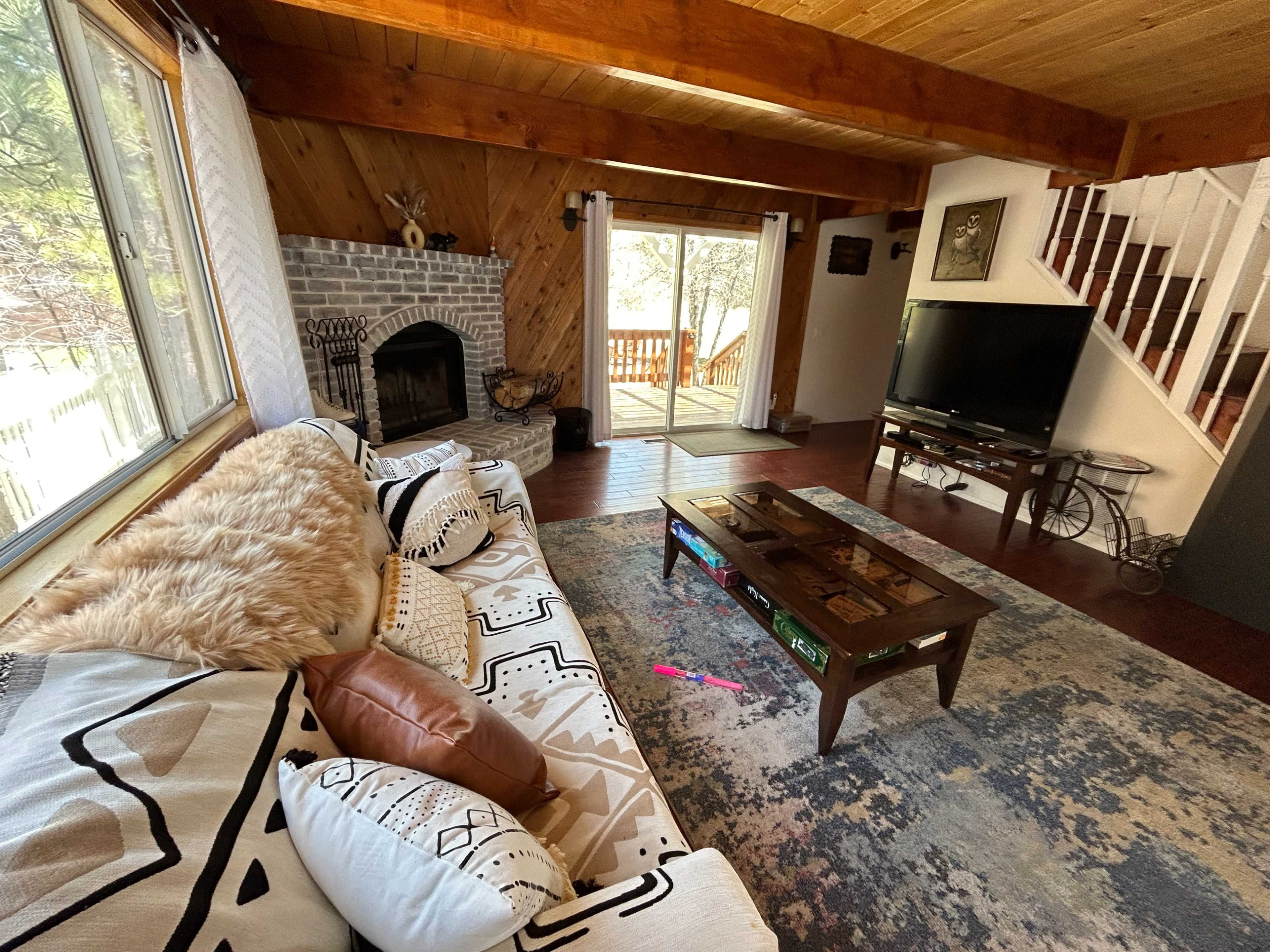 A living room with a large window, a brick fireplace, a wooden coffee table, and a comfortable couch adorned with decorative pillows.