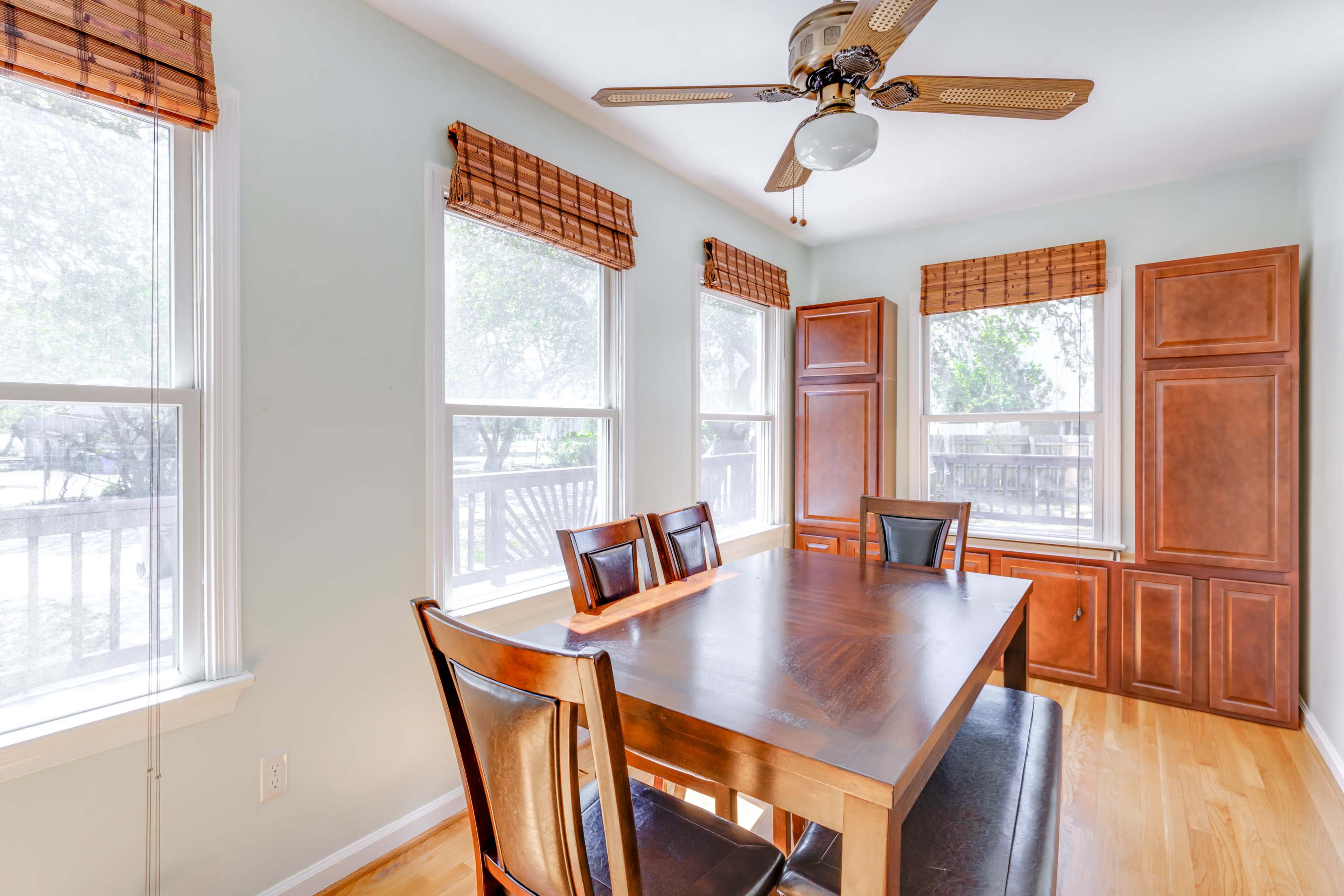 A dining area features a wooden table surrounded by chairs, with windows and light-colored walls enhancing the space.