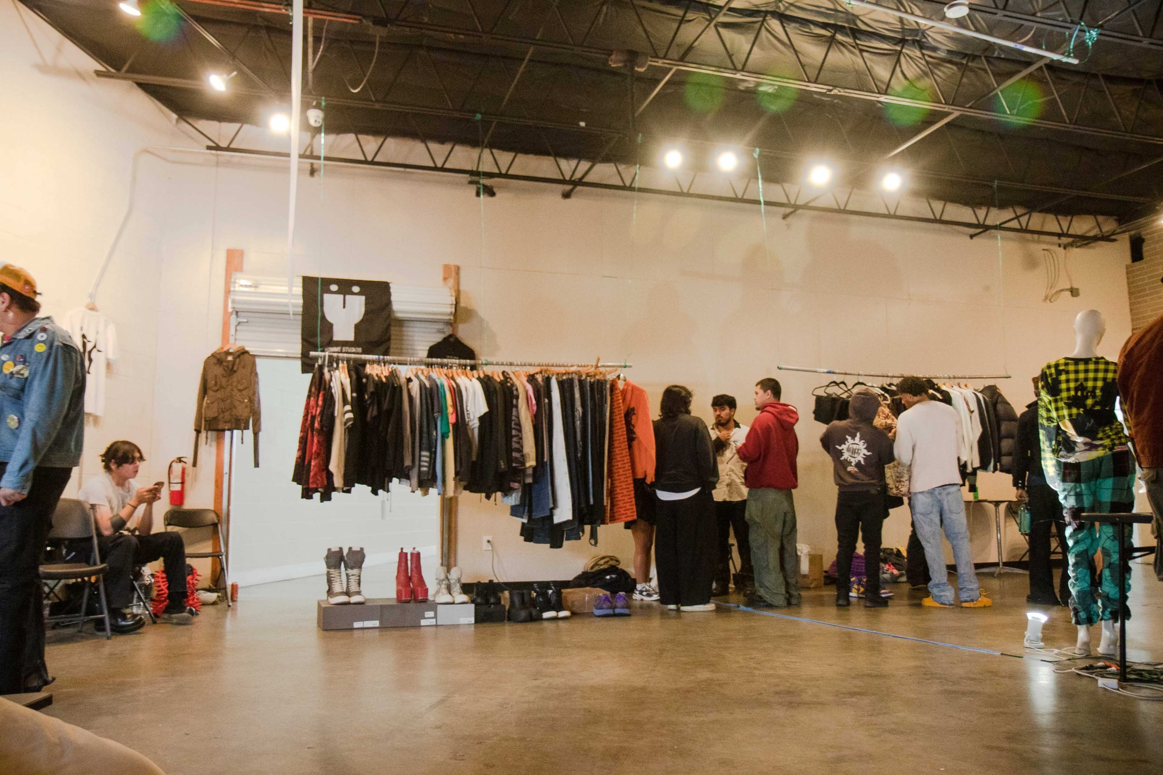 A group of people browse through hanging clothing racks in a spacious retail space with industrial lighting.