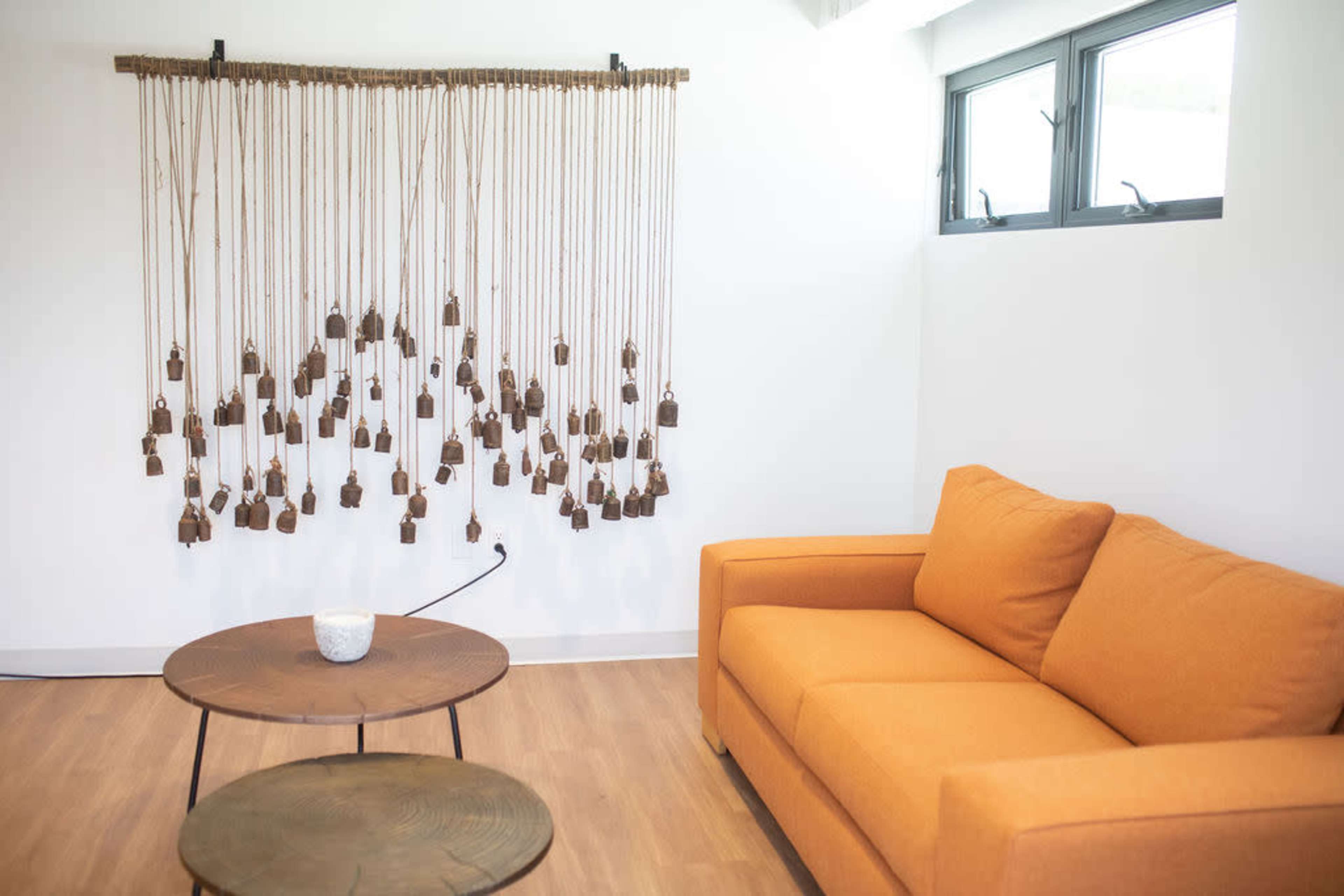 A cozy indoor space features an orange sofa, a wooden coffee table, and a hanging art installation made of small brown bells.