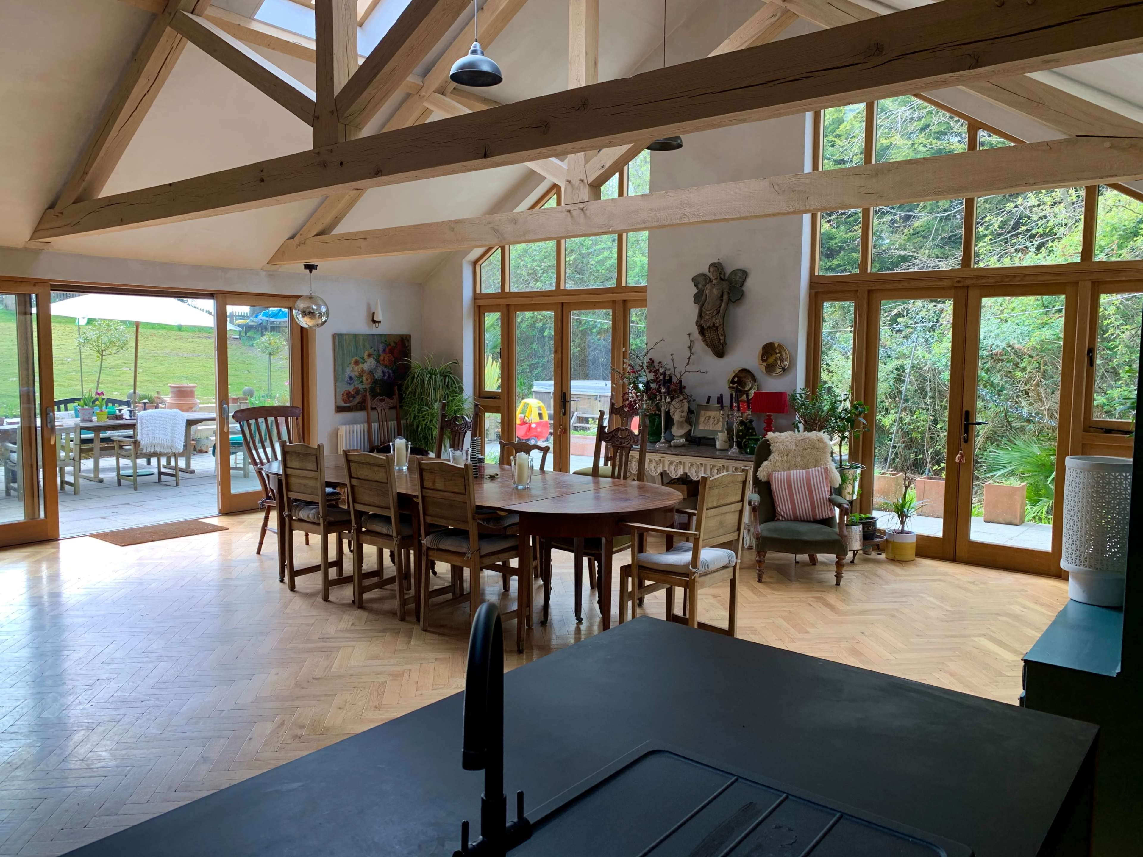 A spacious kitchen features wooden beams, a large dining table surrounded by chairs, and glass doors leading to an outdoor patio.