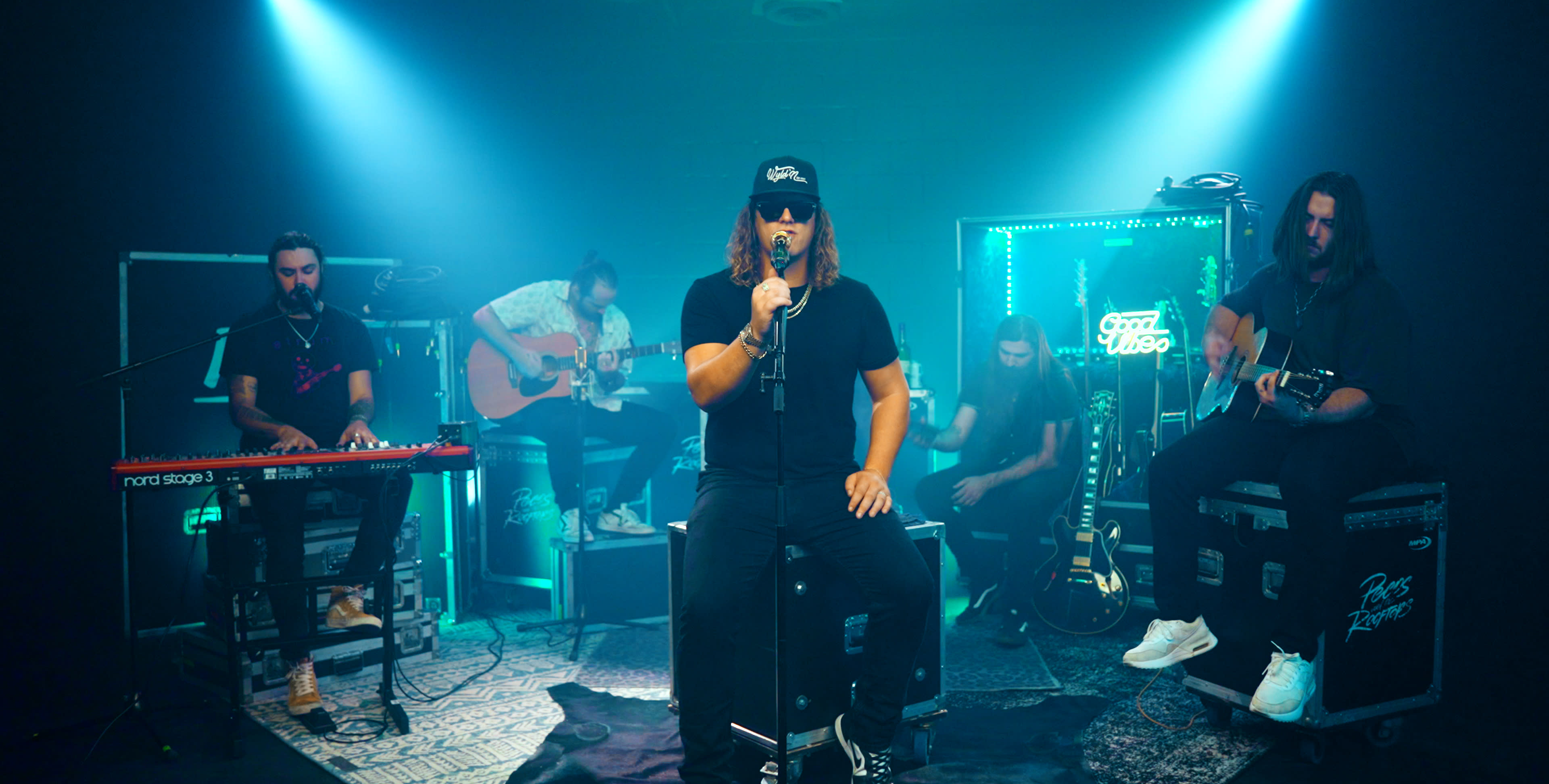 A band performs a live session in a dimly lit studio, surrounded by musical instruments and neon lights.