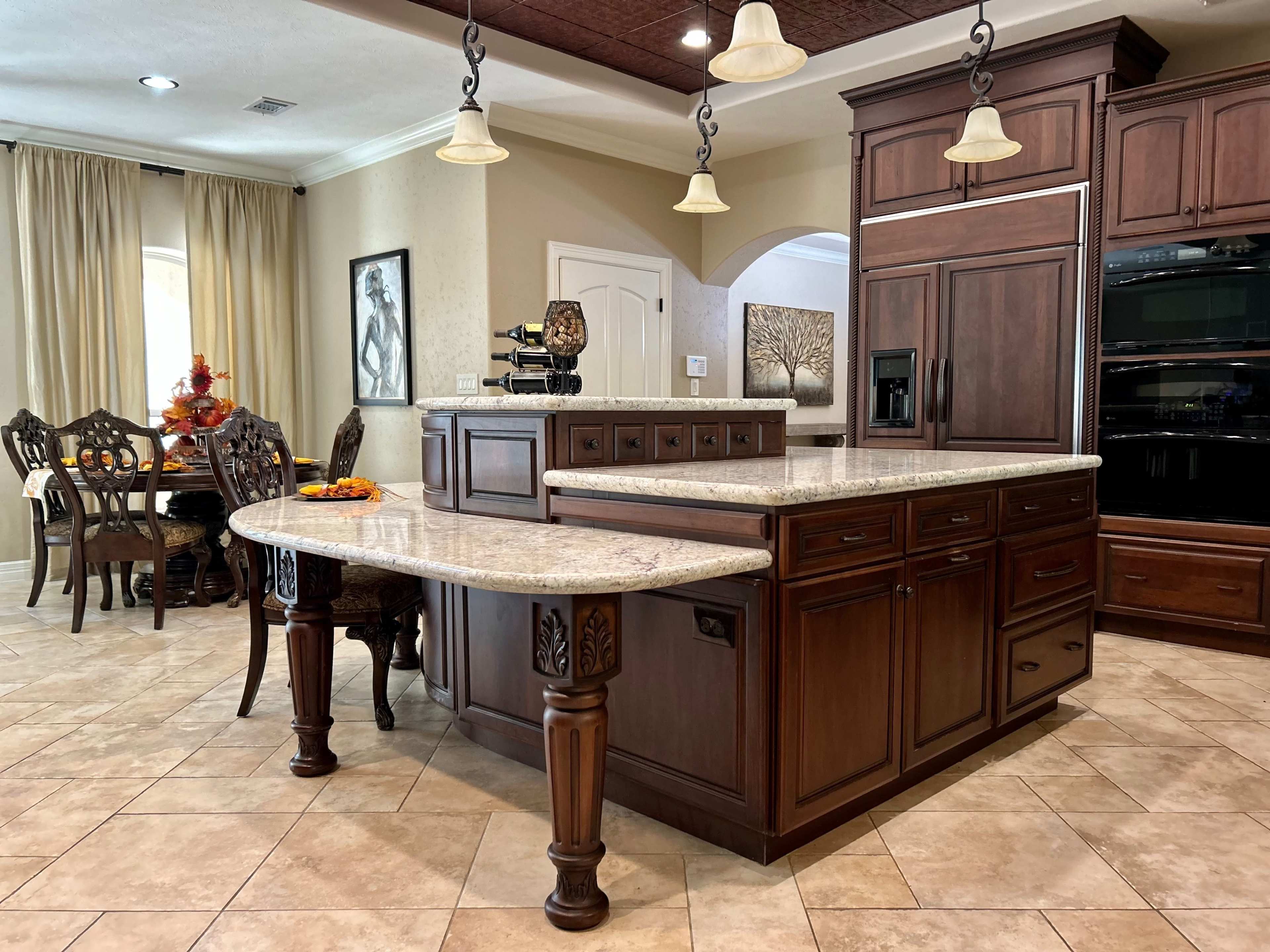 A modern kitchen with dark wood cabinets, a granite countertop, and a dining area in the background.