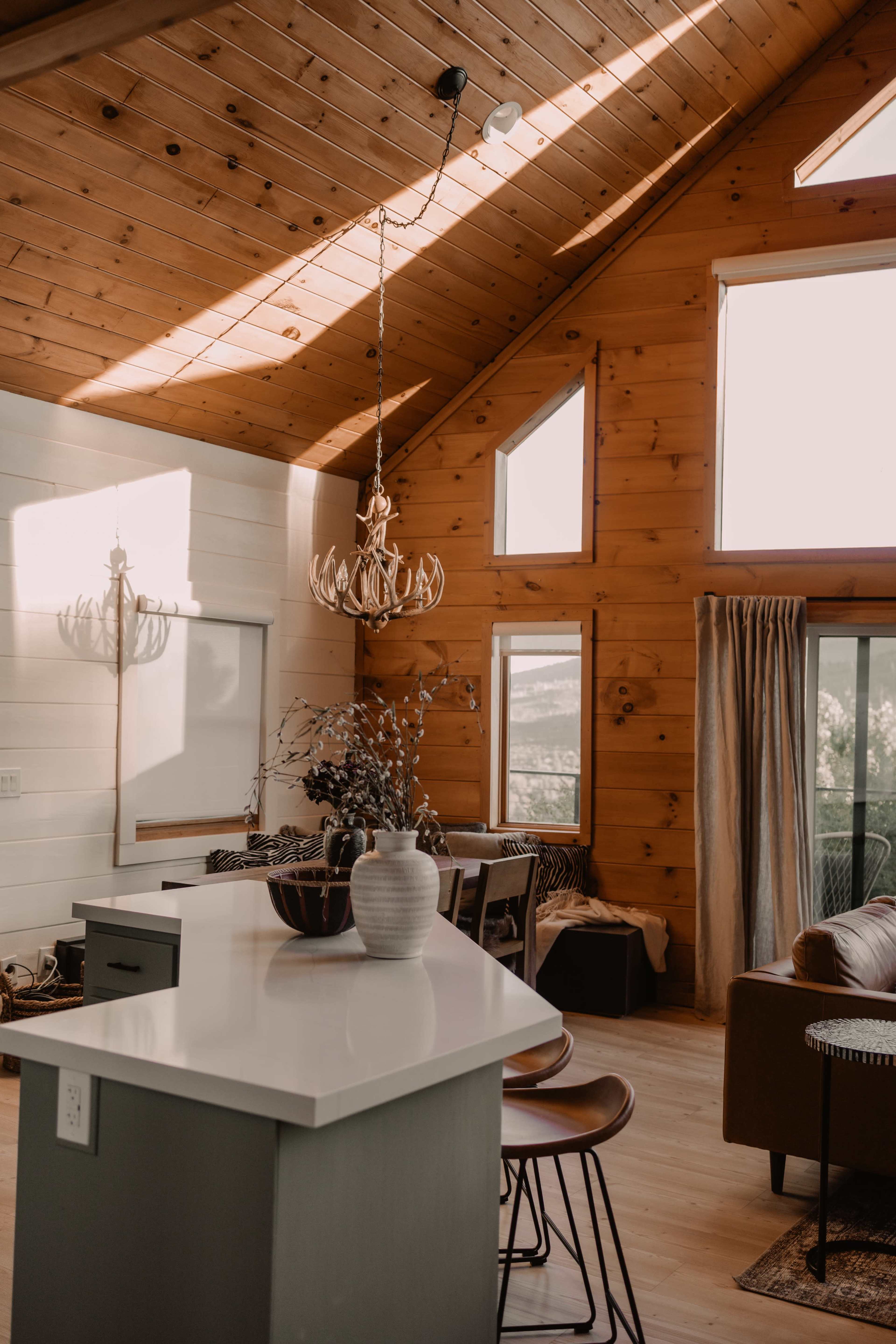 A spacious cabin interior with wooden walls, a large window allowing natural light, and a modern kitchen island with bar stools.