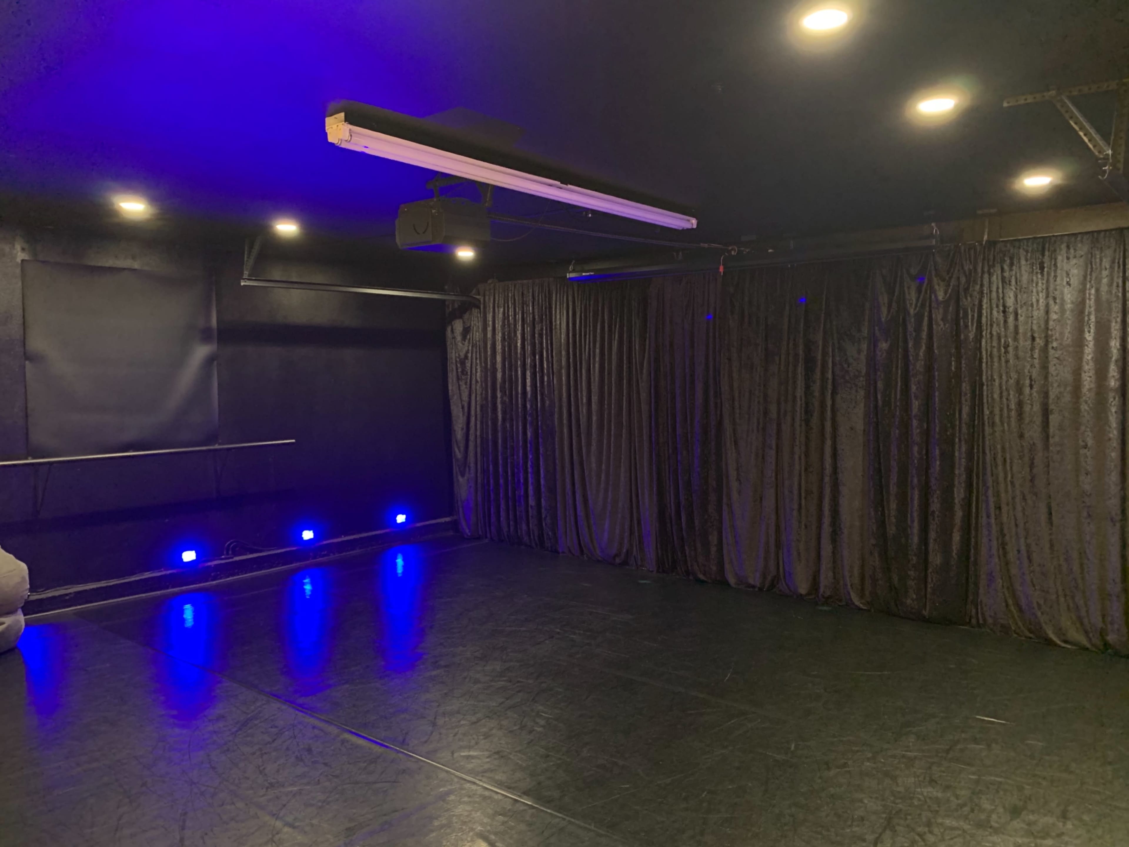 A dimly lit dance studio with black curtains and blue LED lights along the floor.