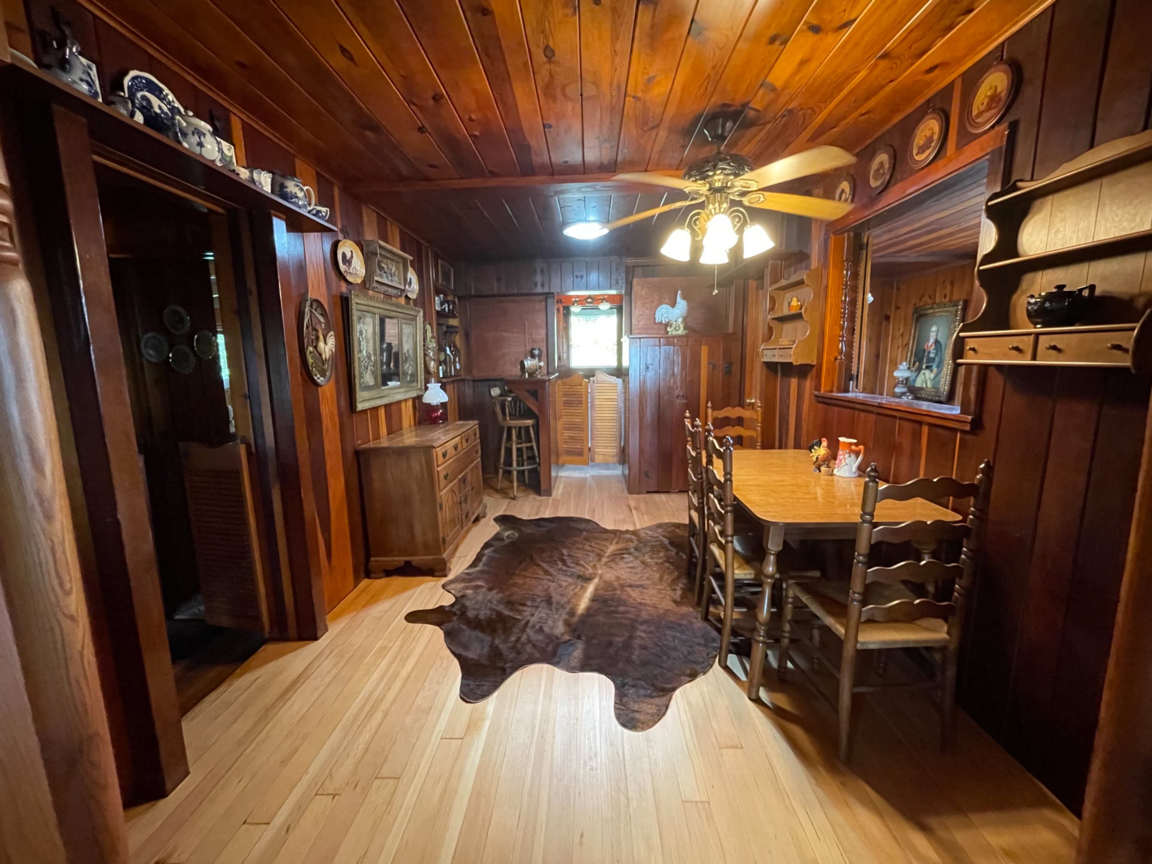 A wooden dining area featuring a table with chairs, a cowhide rug, and various wall decorations.
