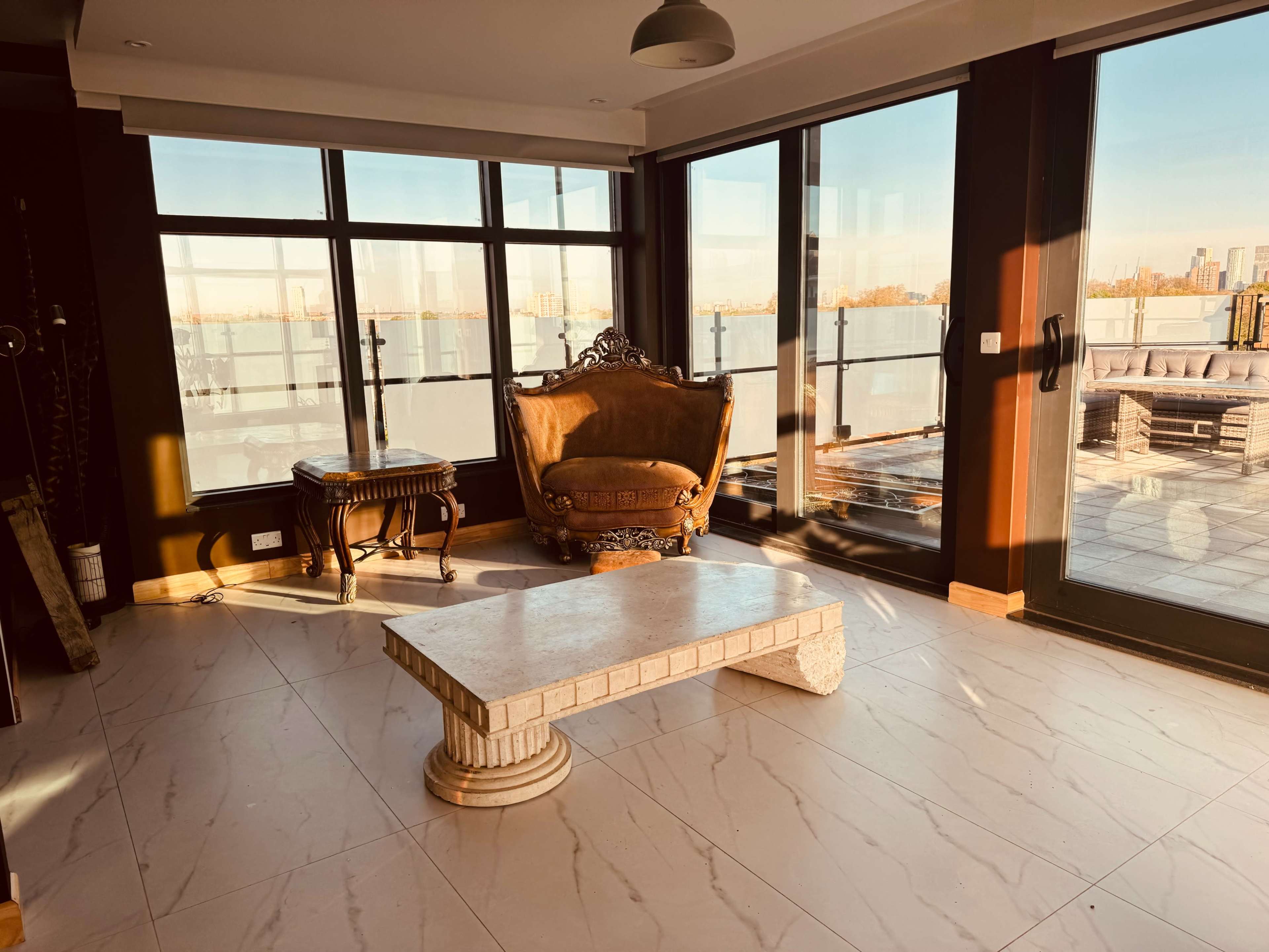 A room with large windows overlooking a cityscape, featuring a decorative armchair and a stone coffee table.