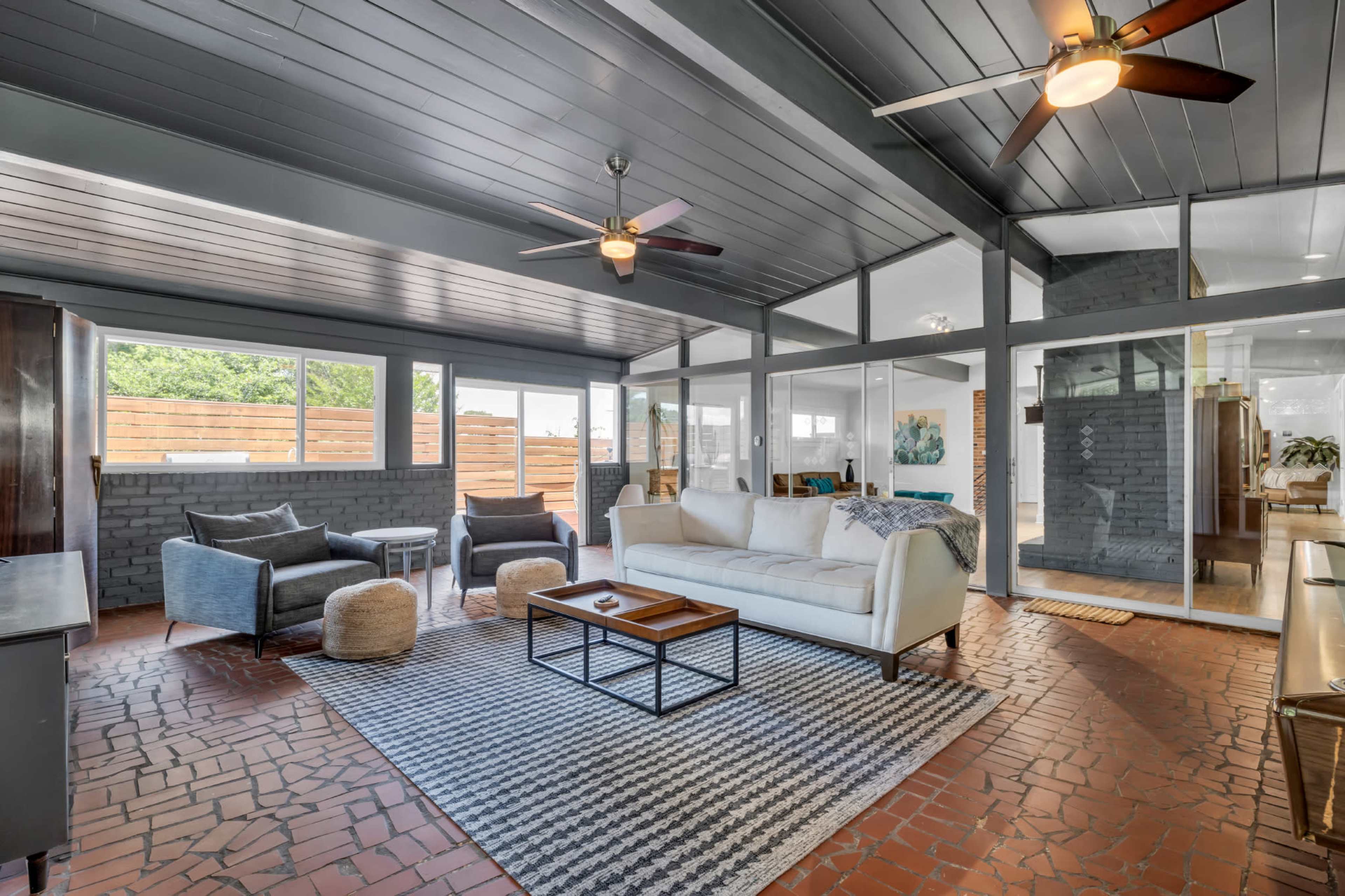 A spacious sunroom with a white sofa, two chairs, a coffee table, and large windows allowing natural light.