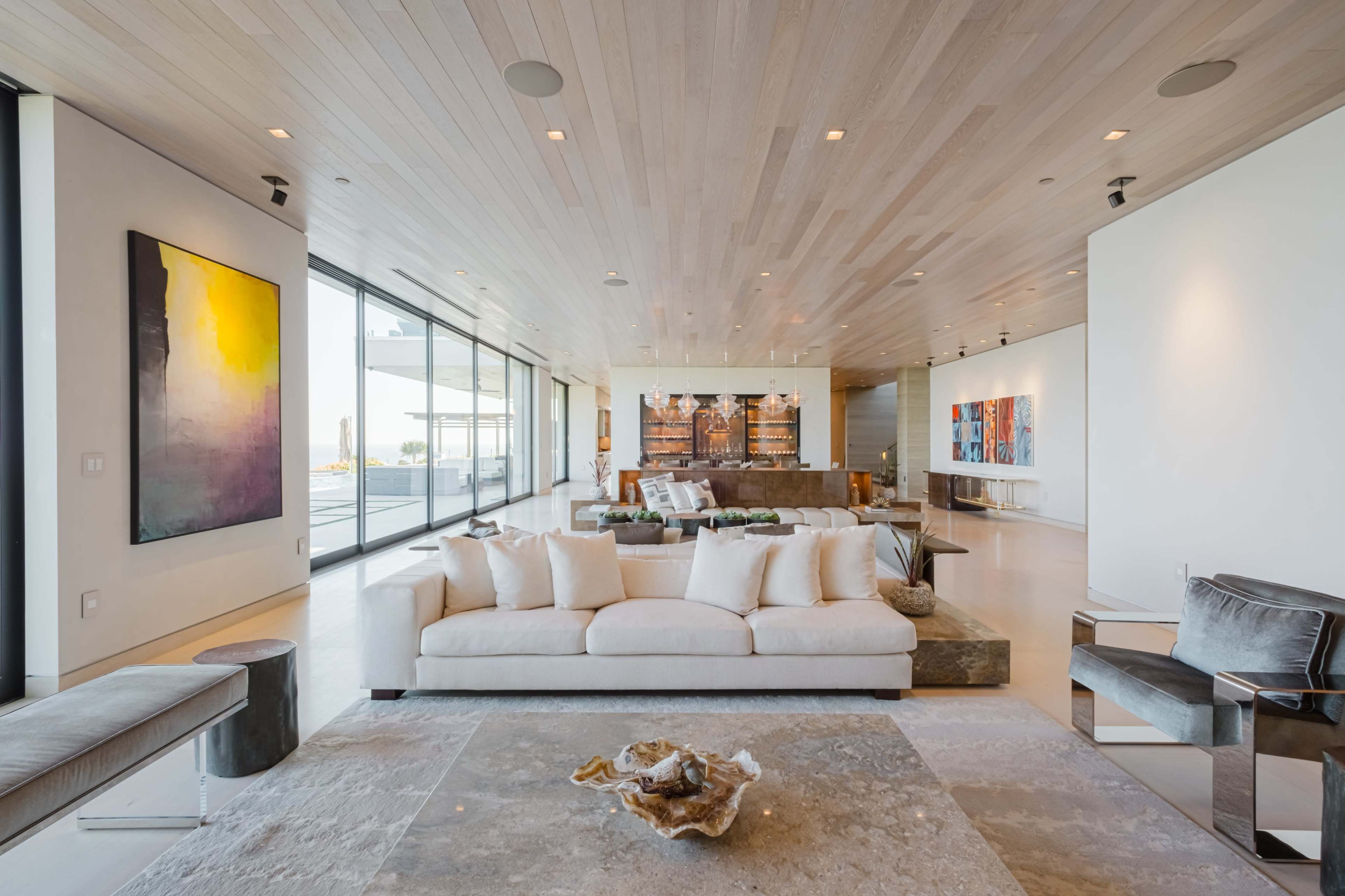 A modern living room with large glass windows, a neutral-colored sofa, and various pieces of artwork on the walls.