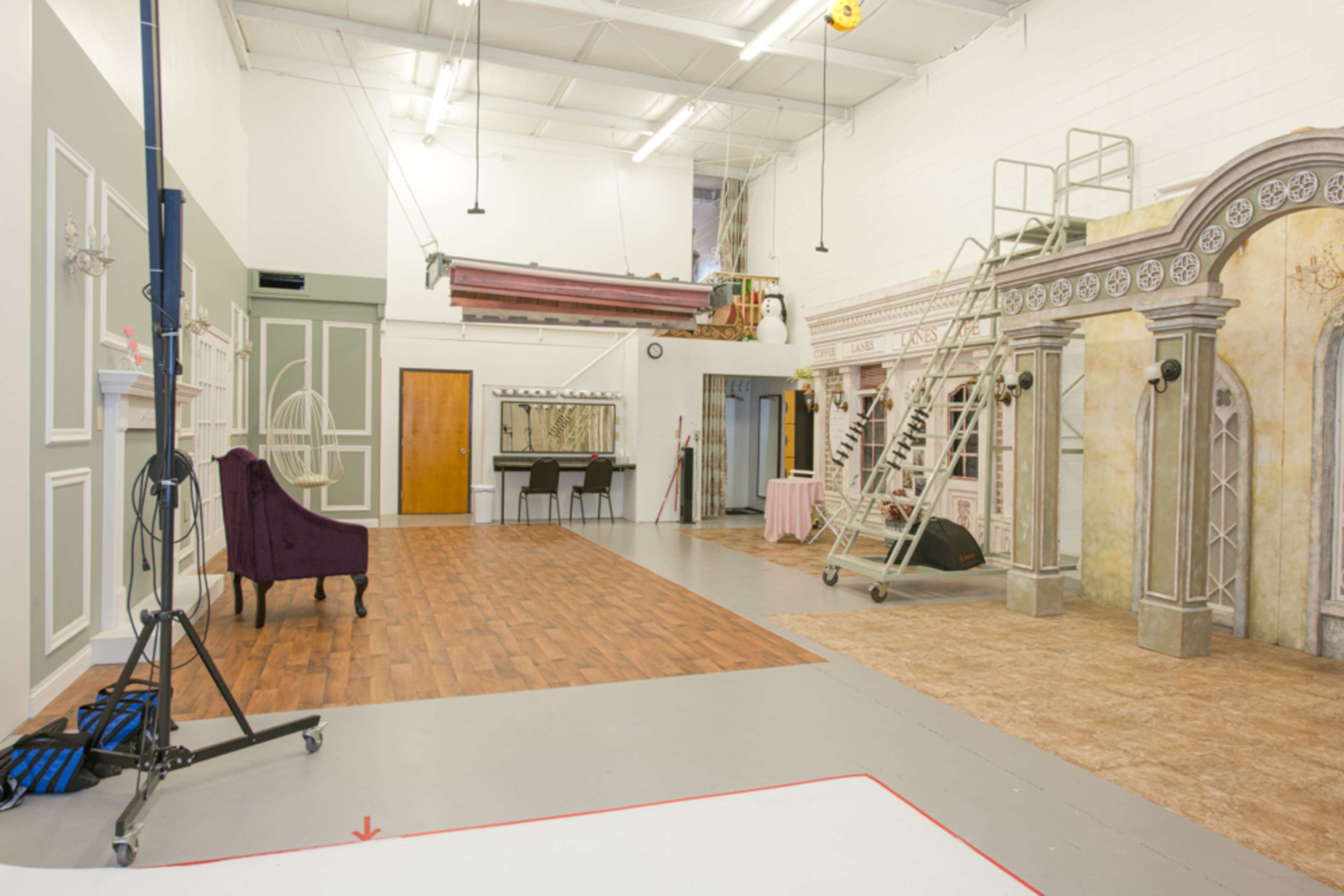 A spacious studio interior featuring decorative backdrops, a ladder, a purple chair, and partitions with various textures and colors.