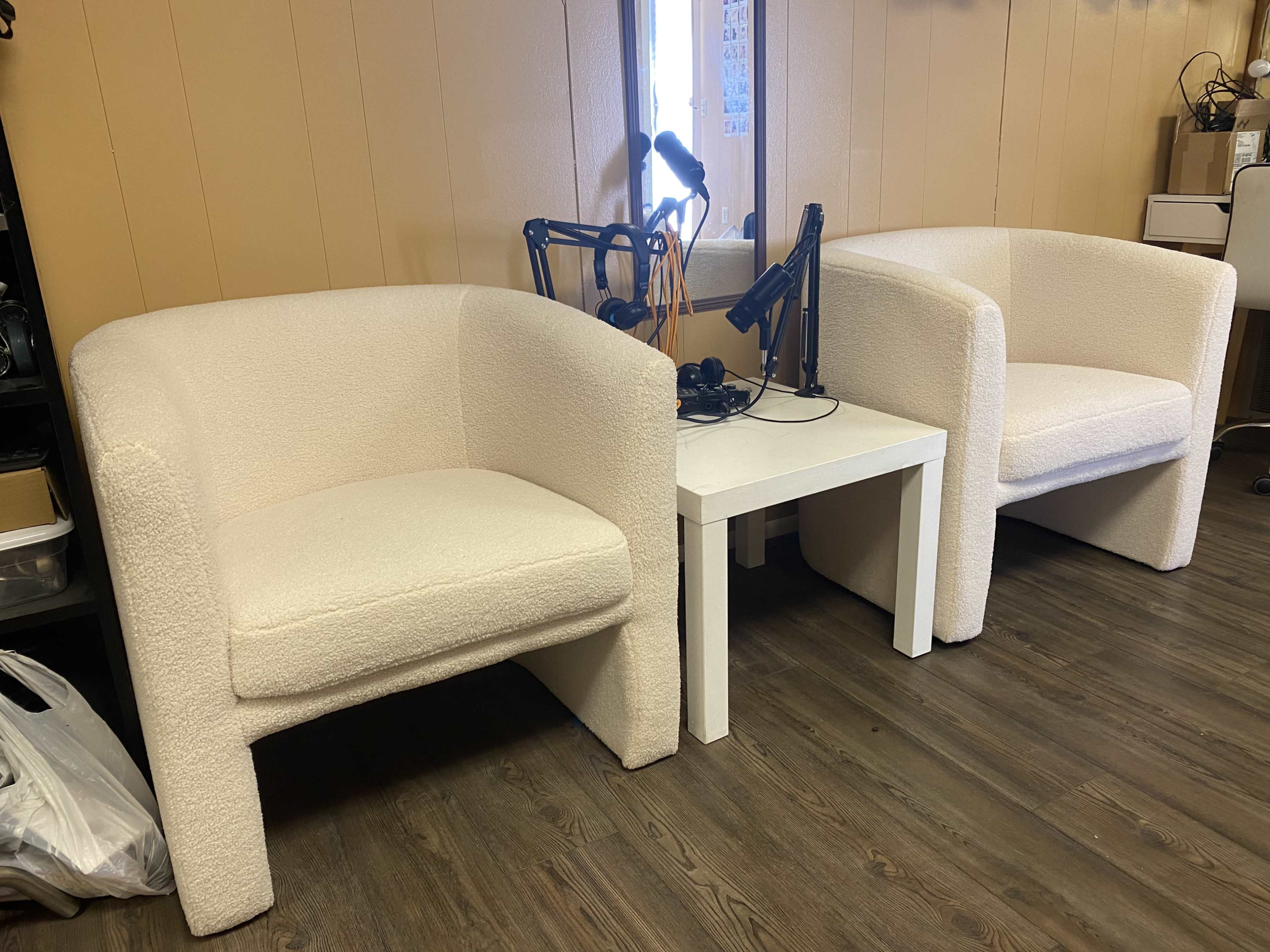The image shows two white upholstered chairs positioned beside a small white table in a room with wooden flooring.