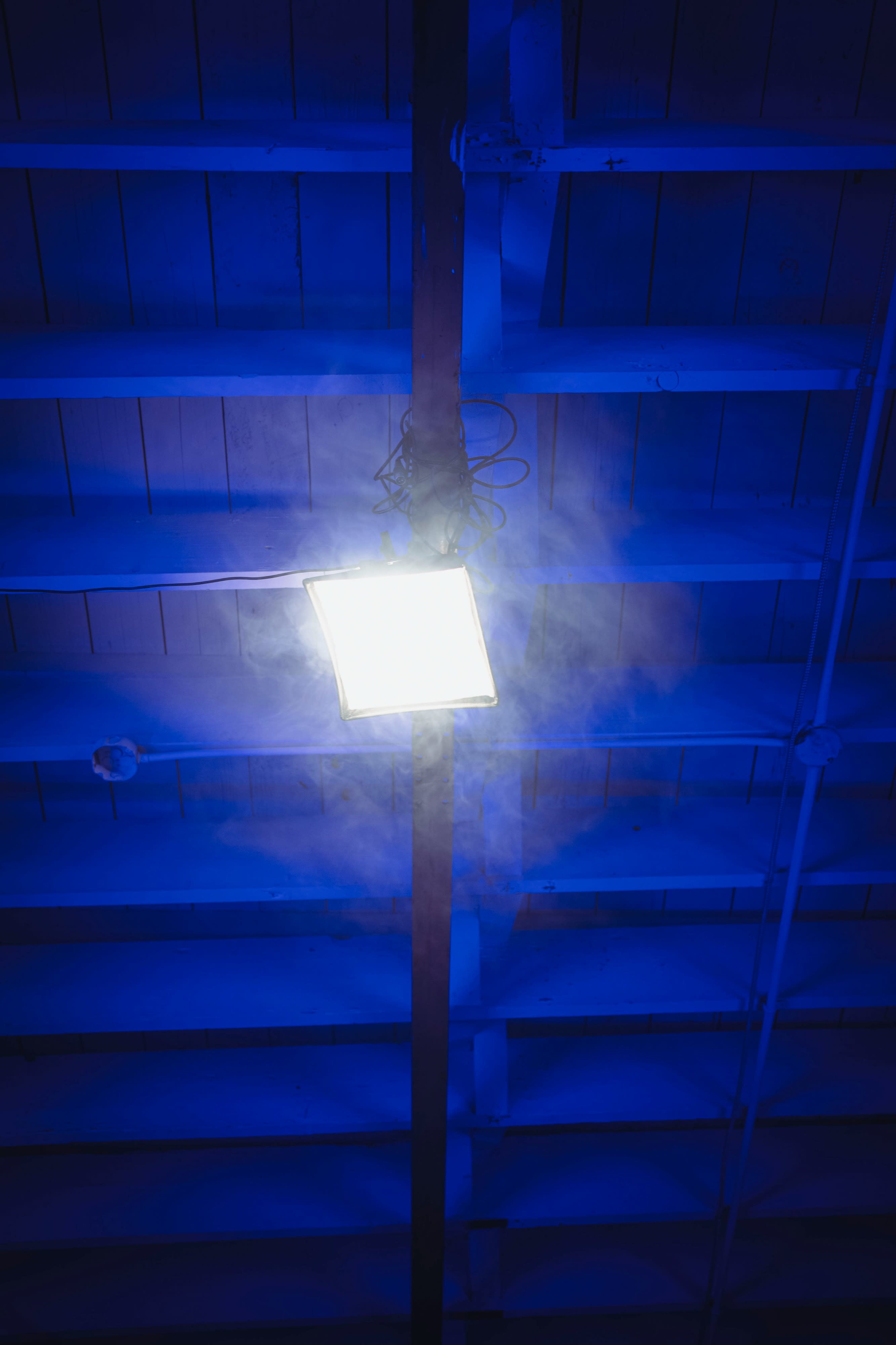 A rectangular light fixture hangs from a beam on a blue ceiling, surrounded by a haze of smoke.