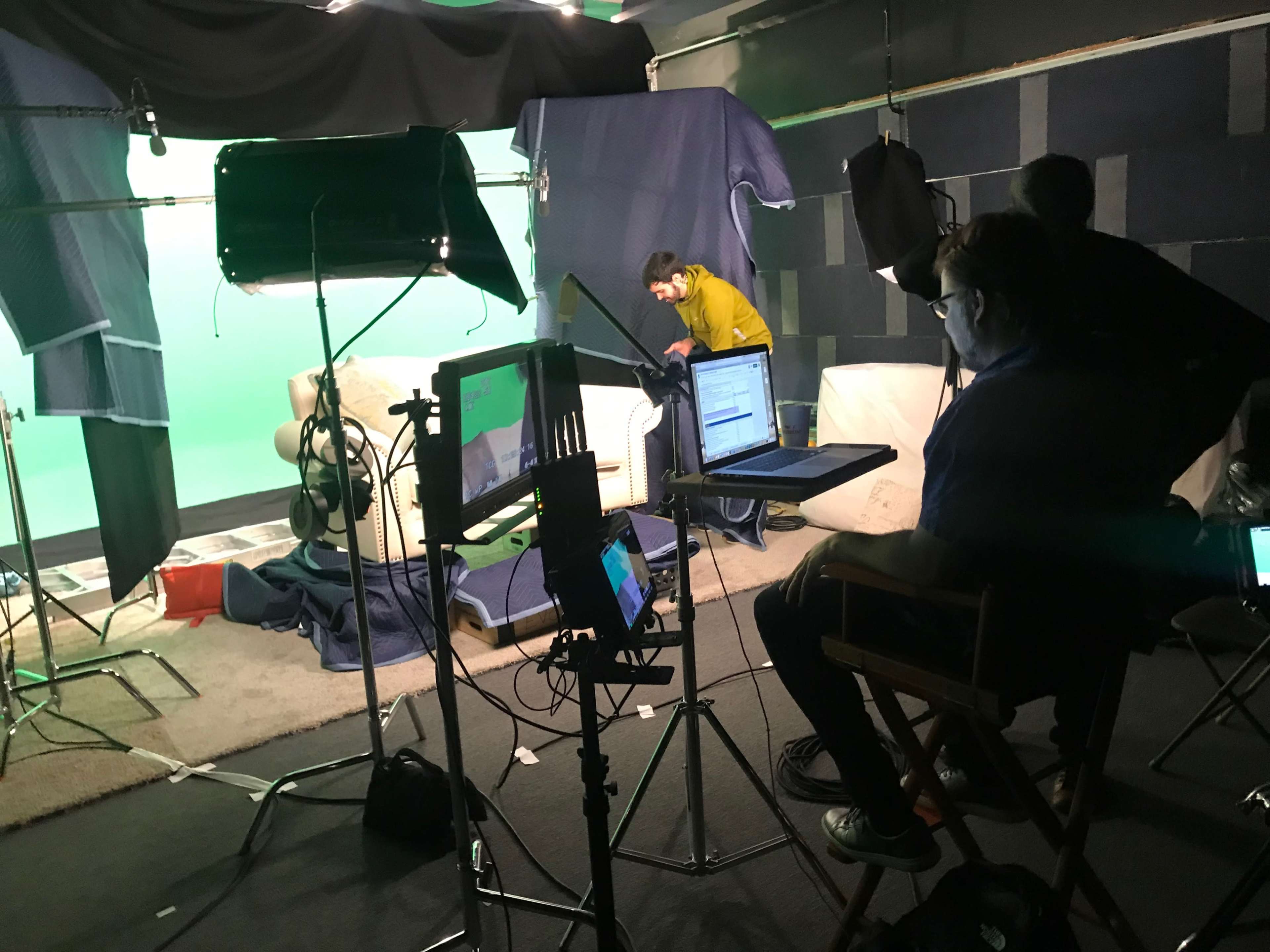 A film set is arranged with a green screen, lighting equipment, and crew members preparing a scene.