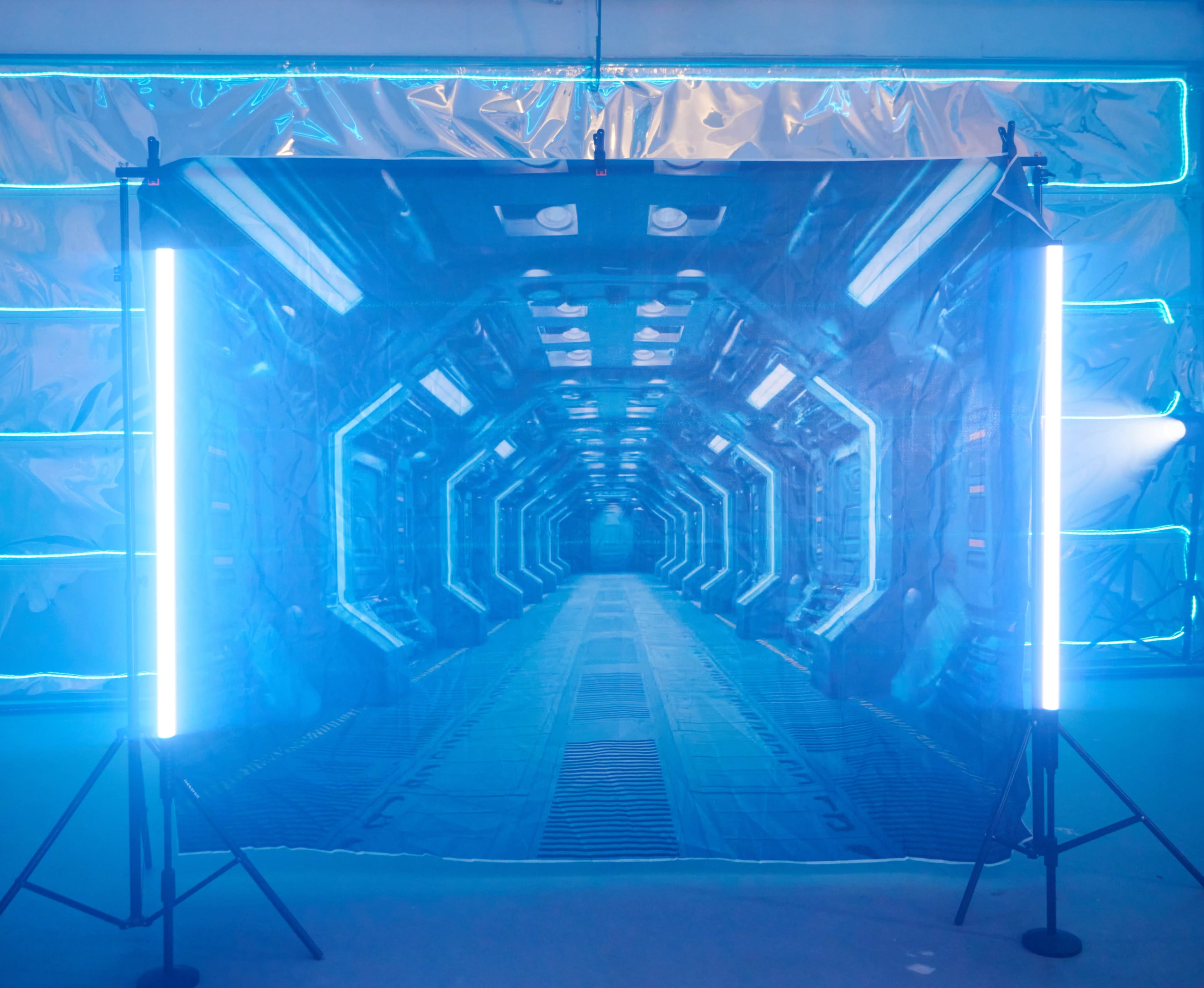 A holographic backdrop depicting a futuristic corridor is illuminated by tall blue lights on either side.