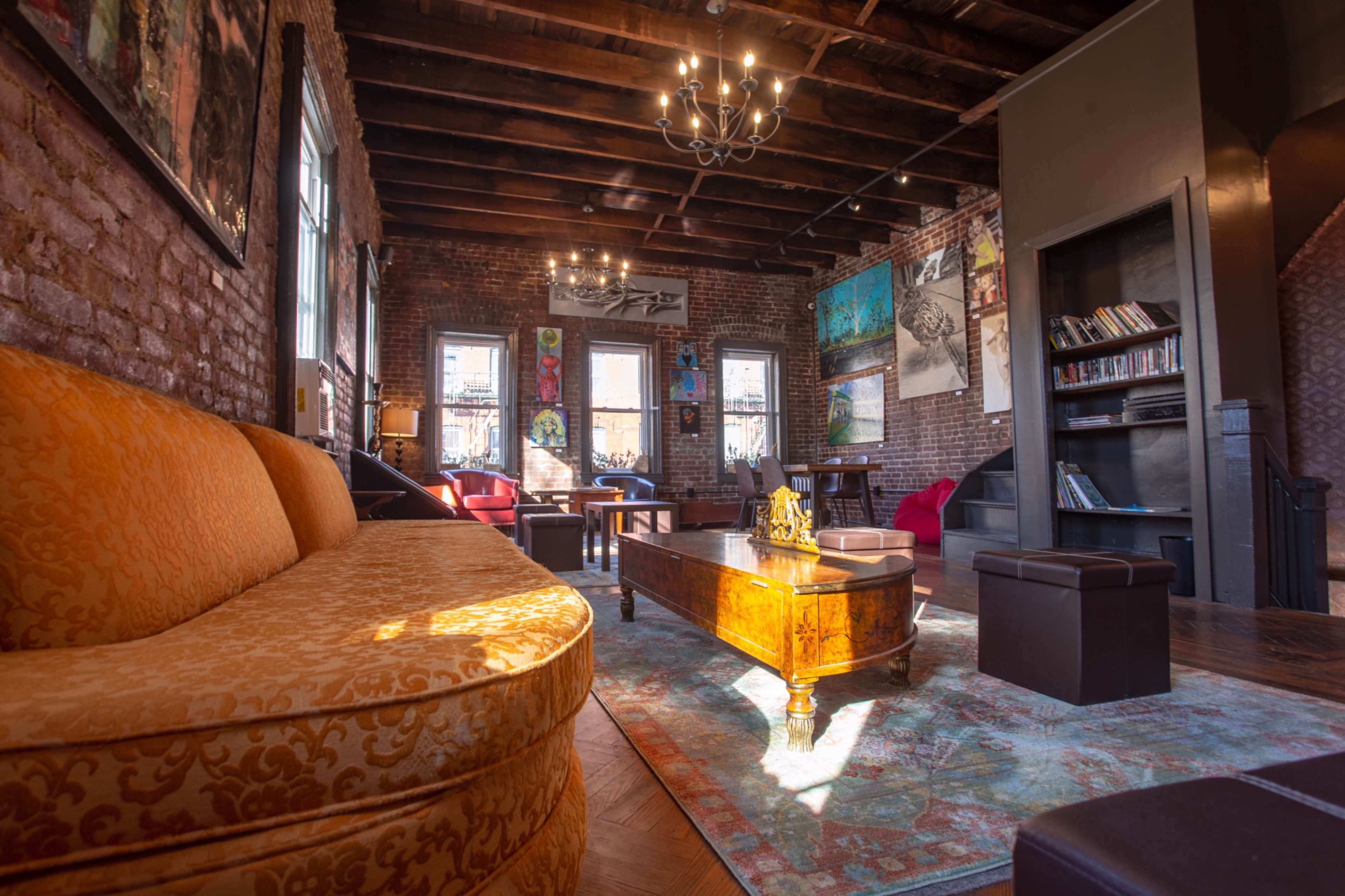 A spacious living room with exposed brick walls, wooden beams, and a mix of seating arrangements, including a large orange couch and coffee tables.