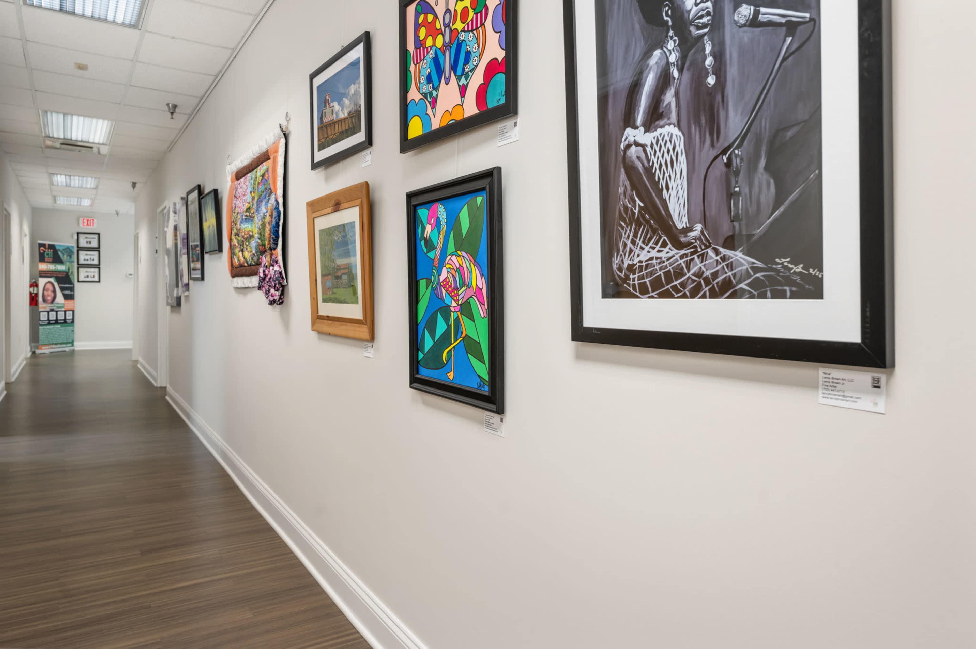 A hallway lined with various framed artworks on the walls, showcasing colorful paintings and photographs.
