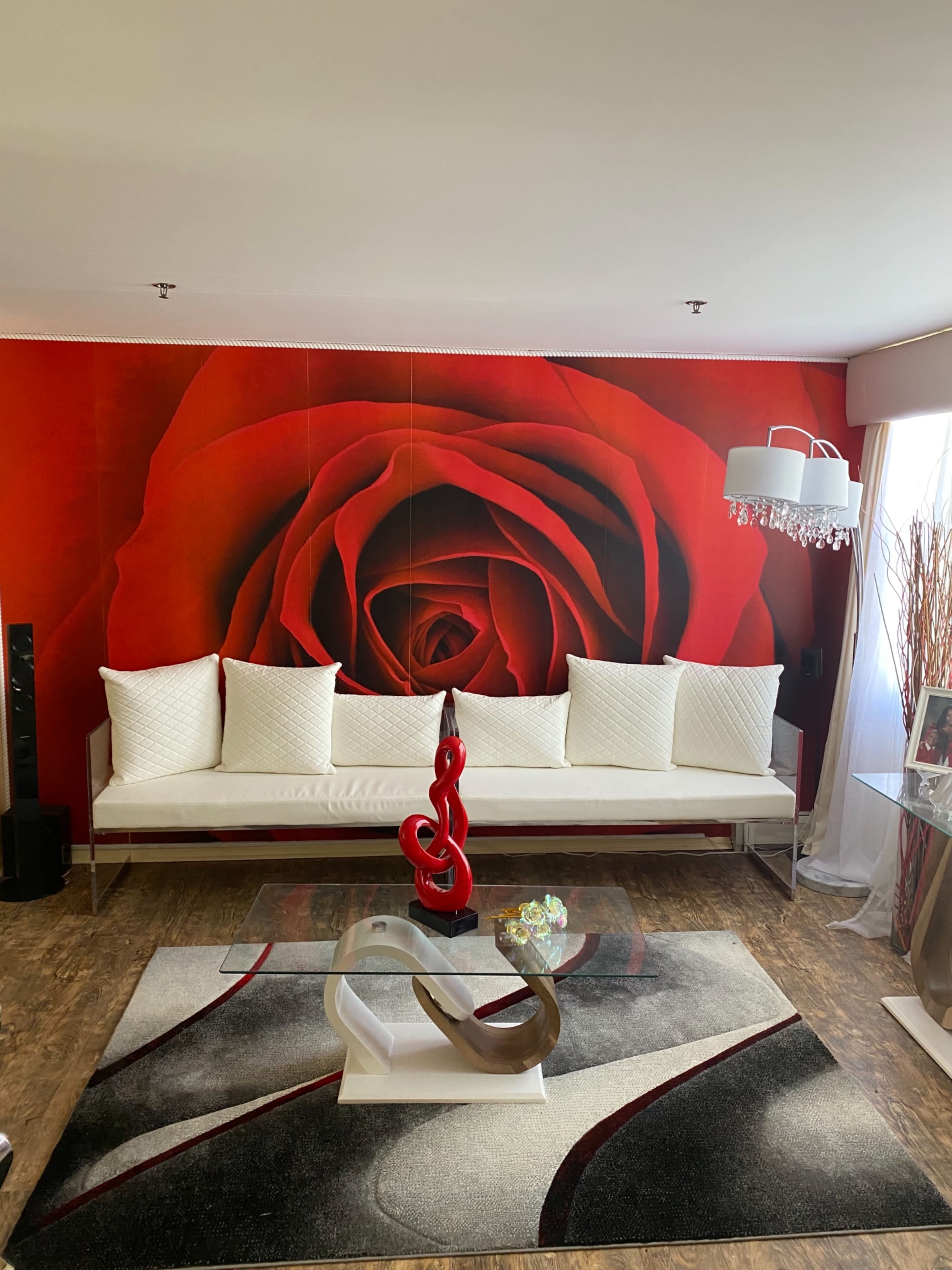The living room features a large red rose mural, a white couch with decorative cushions, a glass coffee table, and a decorative sculpture on a patterned rug.