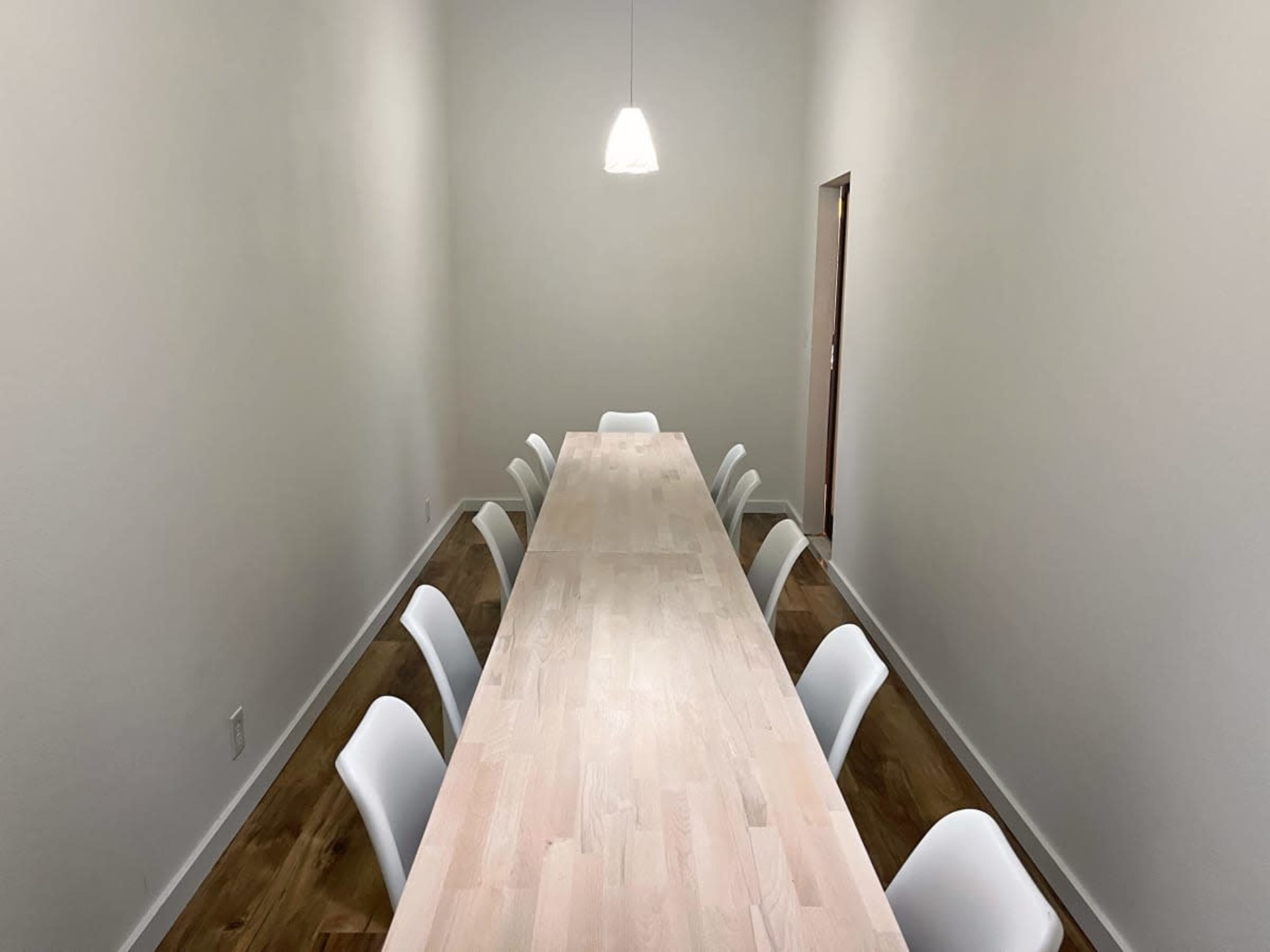 A long wooden table is positioned in a narrow room with white walls and a single pendant light overhead.