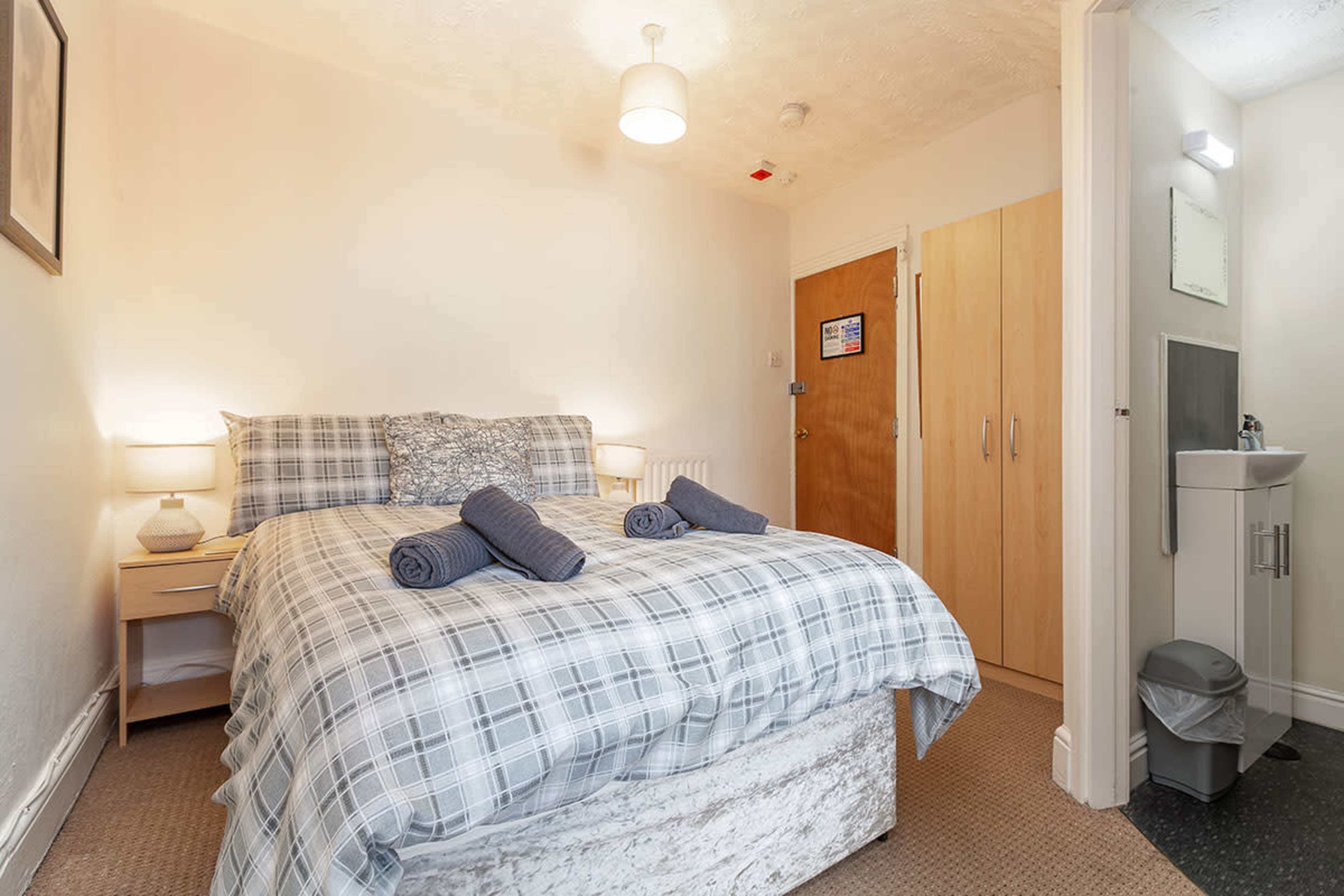 A small bedroom with a double bed, two bedside lamps, and an en-suite bathroom visible in the corner.