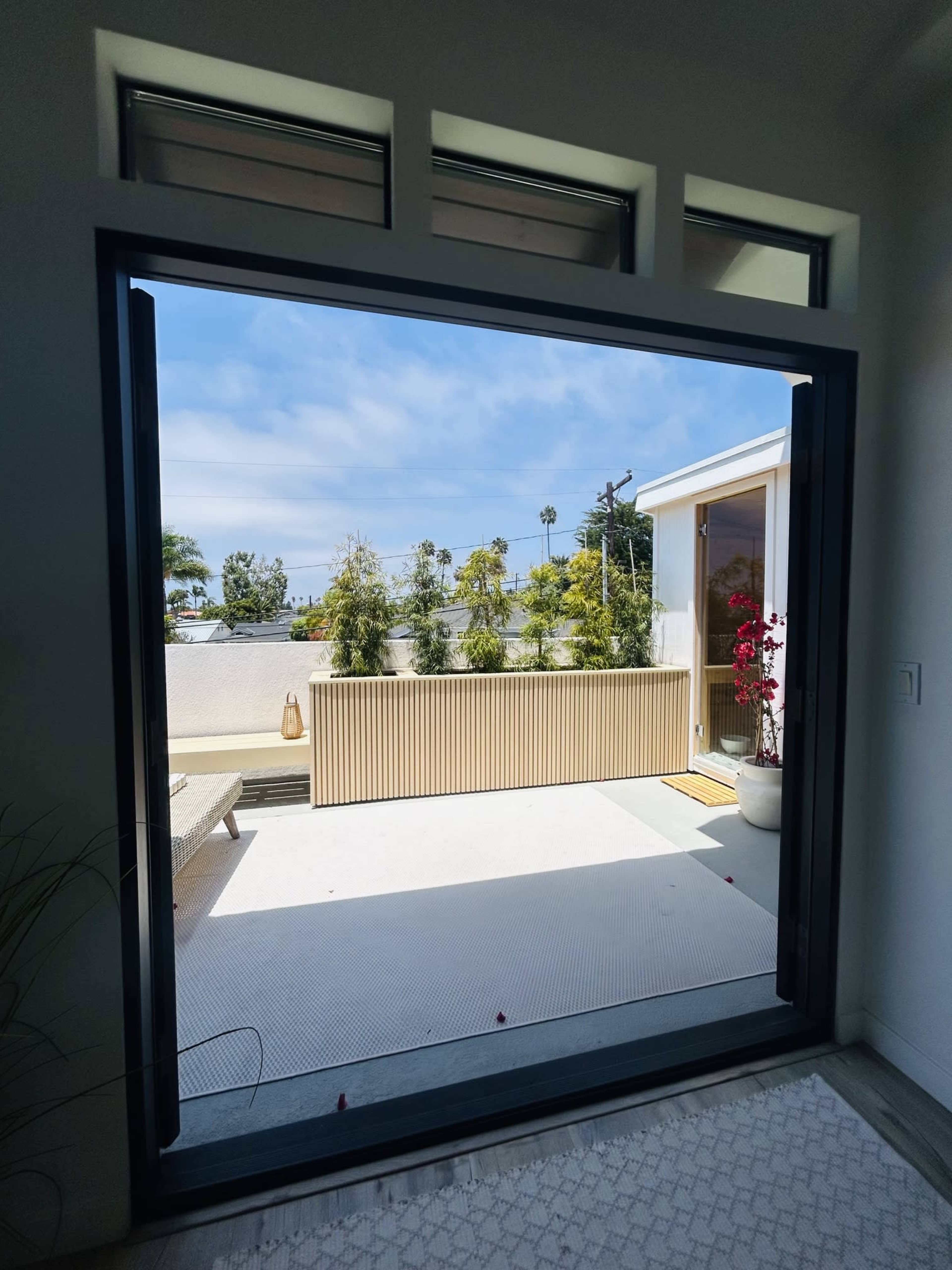A wide open sliding door reveals a patio with potted plants and a clear blue sky.