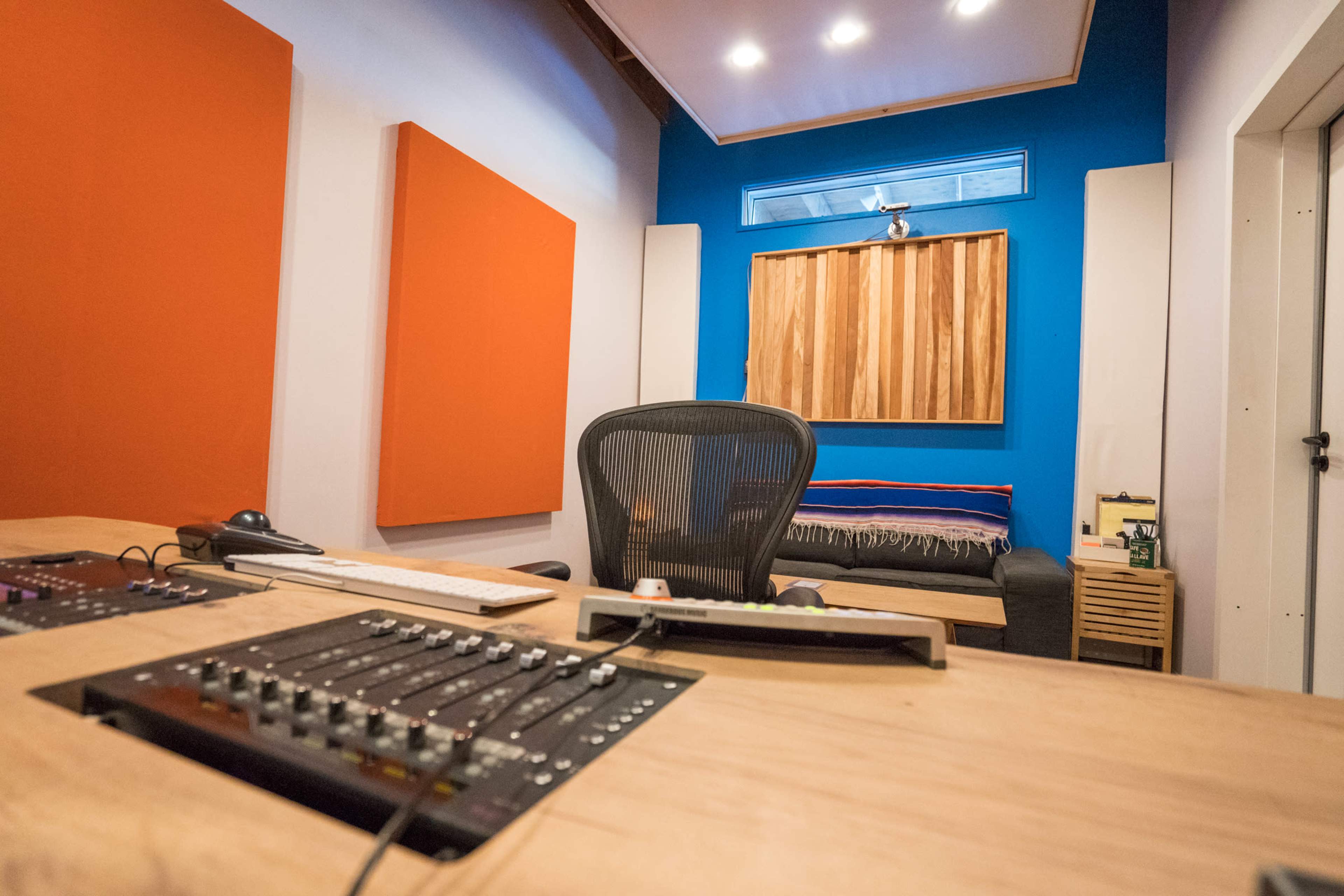 A recording studio with a wooden control desk, an ergonomic chair, and soundproofing panels on the walls.