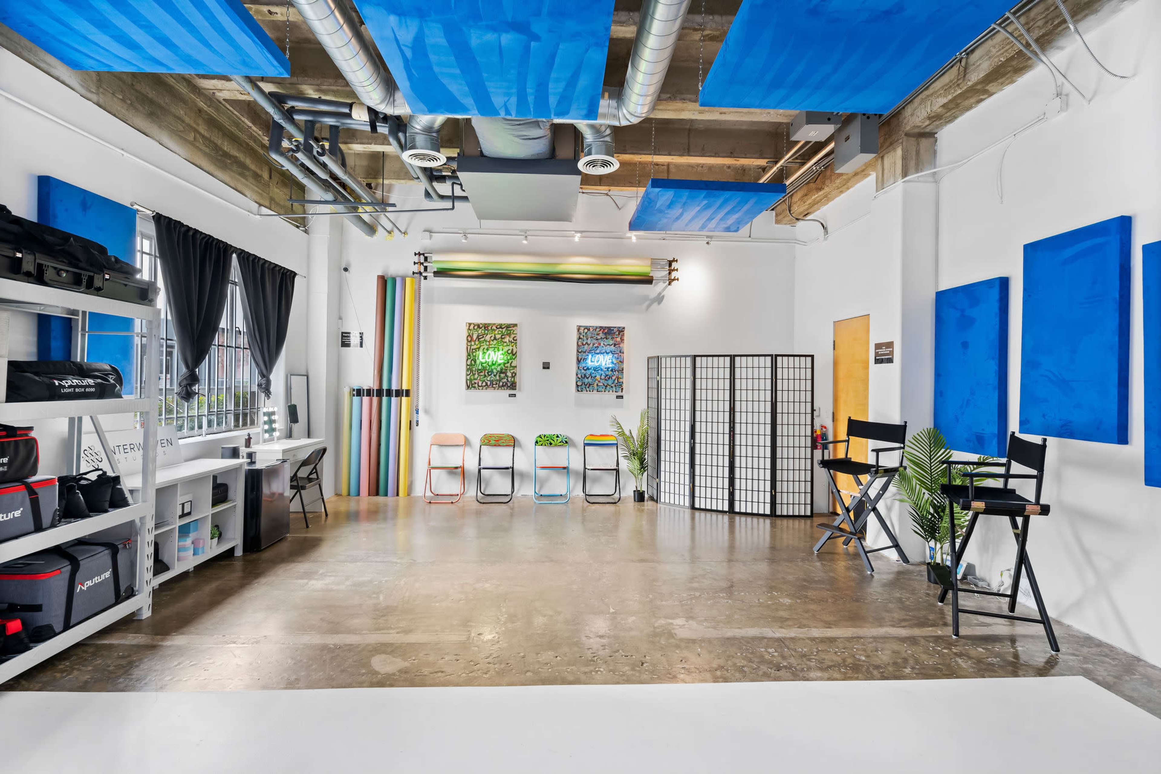 A spacious studio features a polished concrete floor, shelving with equipment, colorful fabric panels on the walls, and a divider with seating areas.