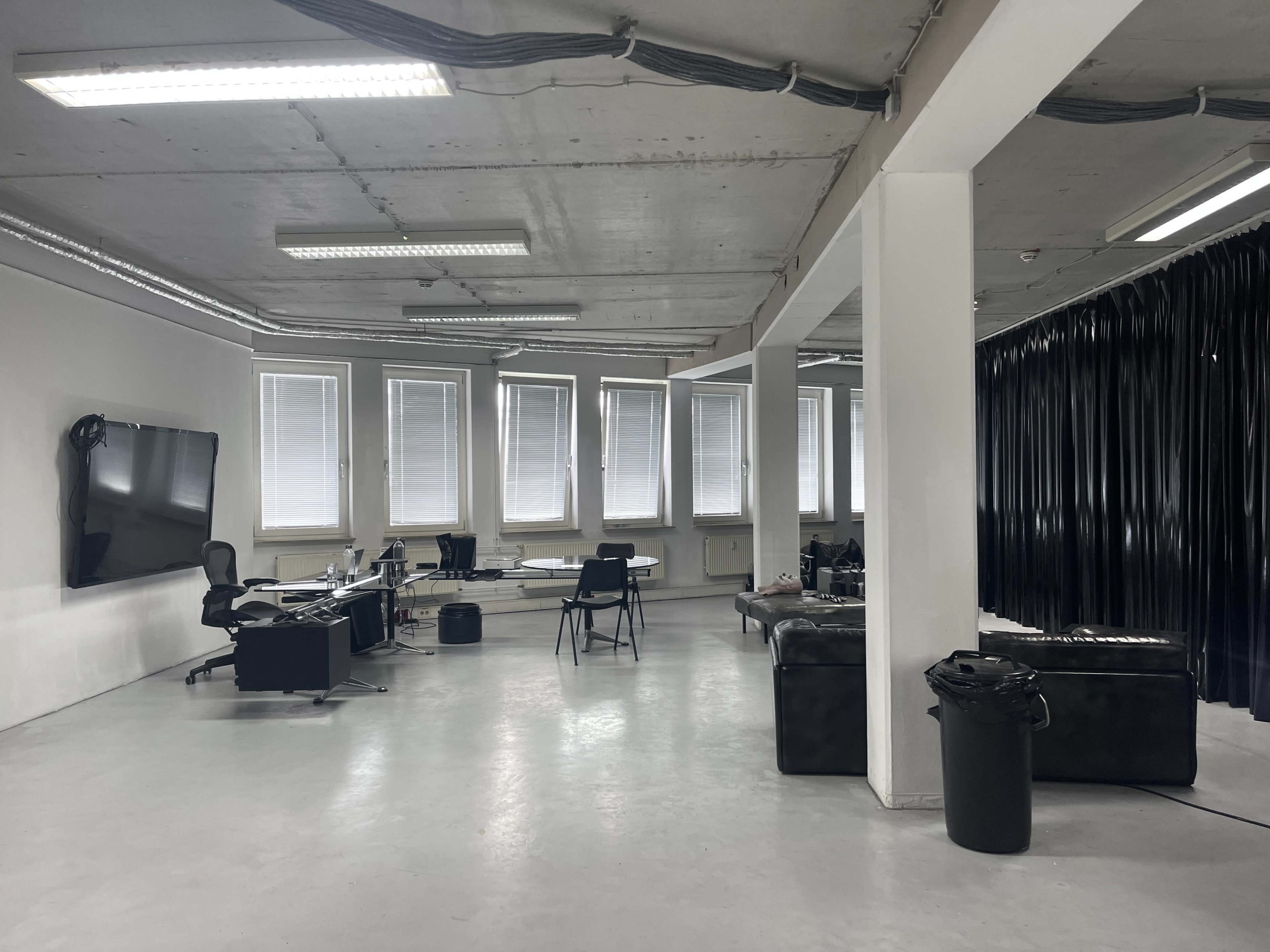 An office space with desks, a large screen, and black curtains lining one wall.